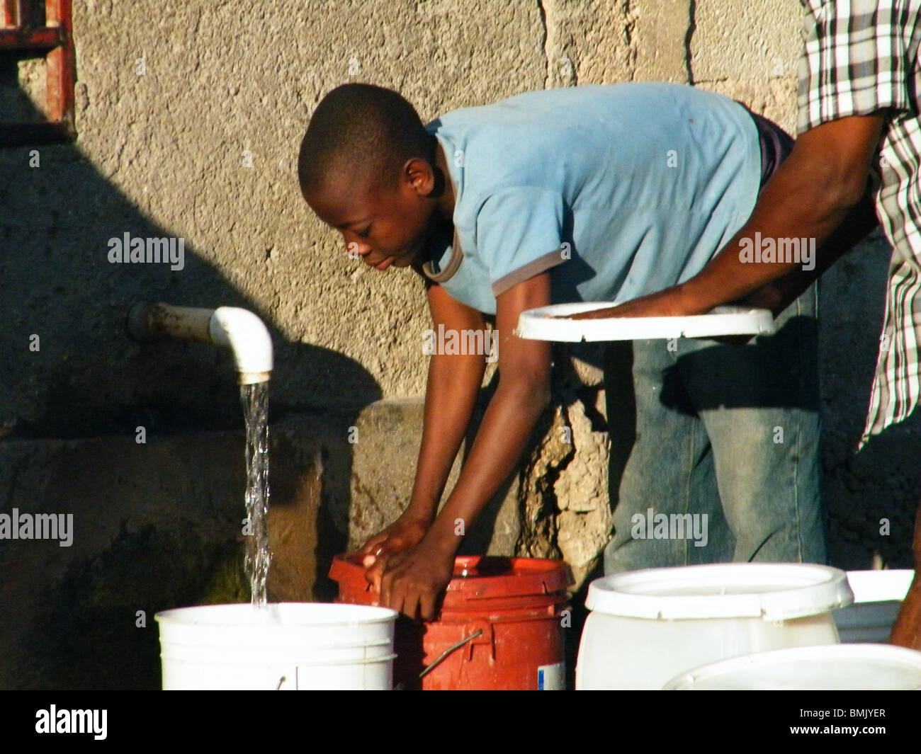 Ein haitianischer junge füllt Eimer mit sauberem Wasser in den frühen Morgenstunden, Gonaives, Haiti Stockfoto