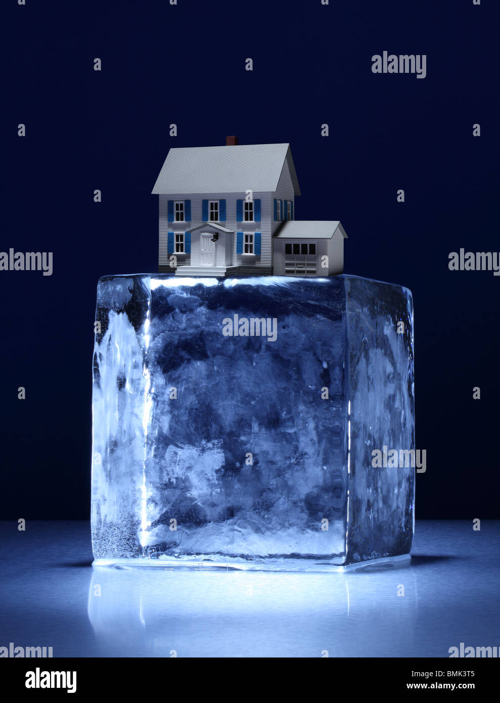 Einen gefrorenen Eisblock mit einem kleinen Modellhaus an der Spitze auf einer Metalloberfläche Stockfoto