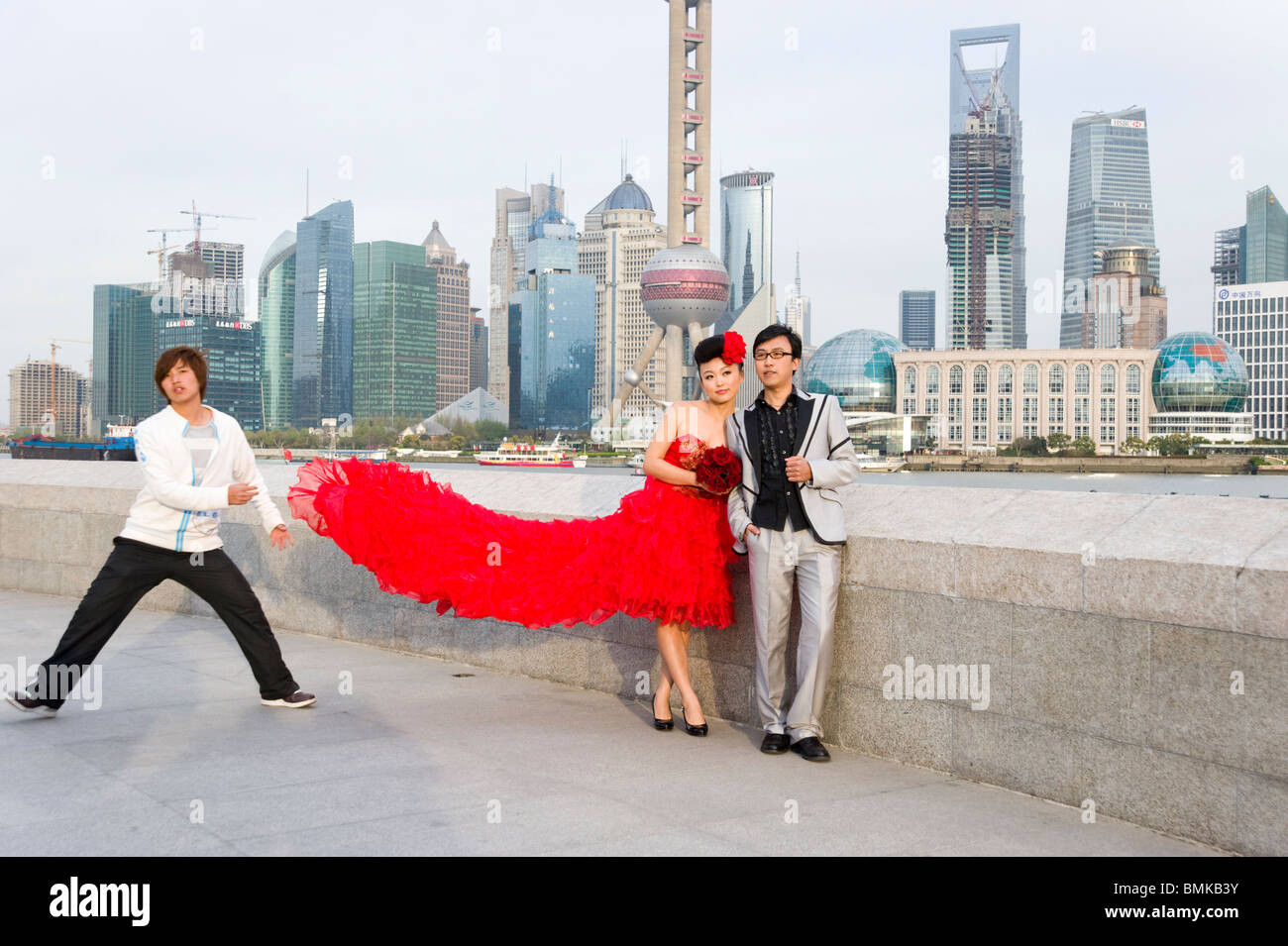 Junge frisch vermählte Paar mit Fotos, auf den Bund gegen die Skyline der Stadt Shanghai, China Stockfoto