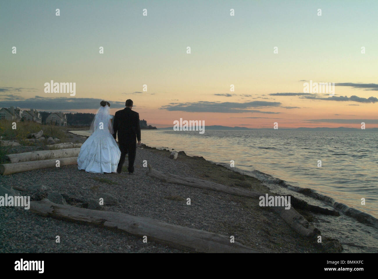 Braut und Bräutigam zu Fuß entlang der Küste in der Abenddämmerung Stockfoto