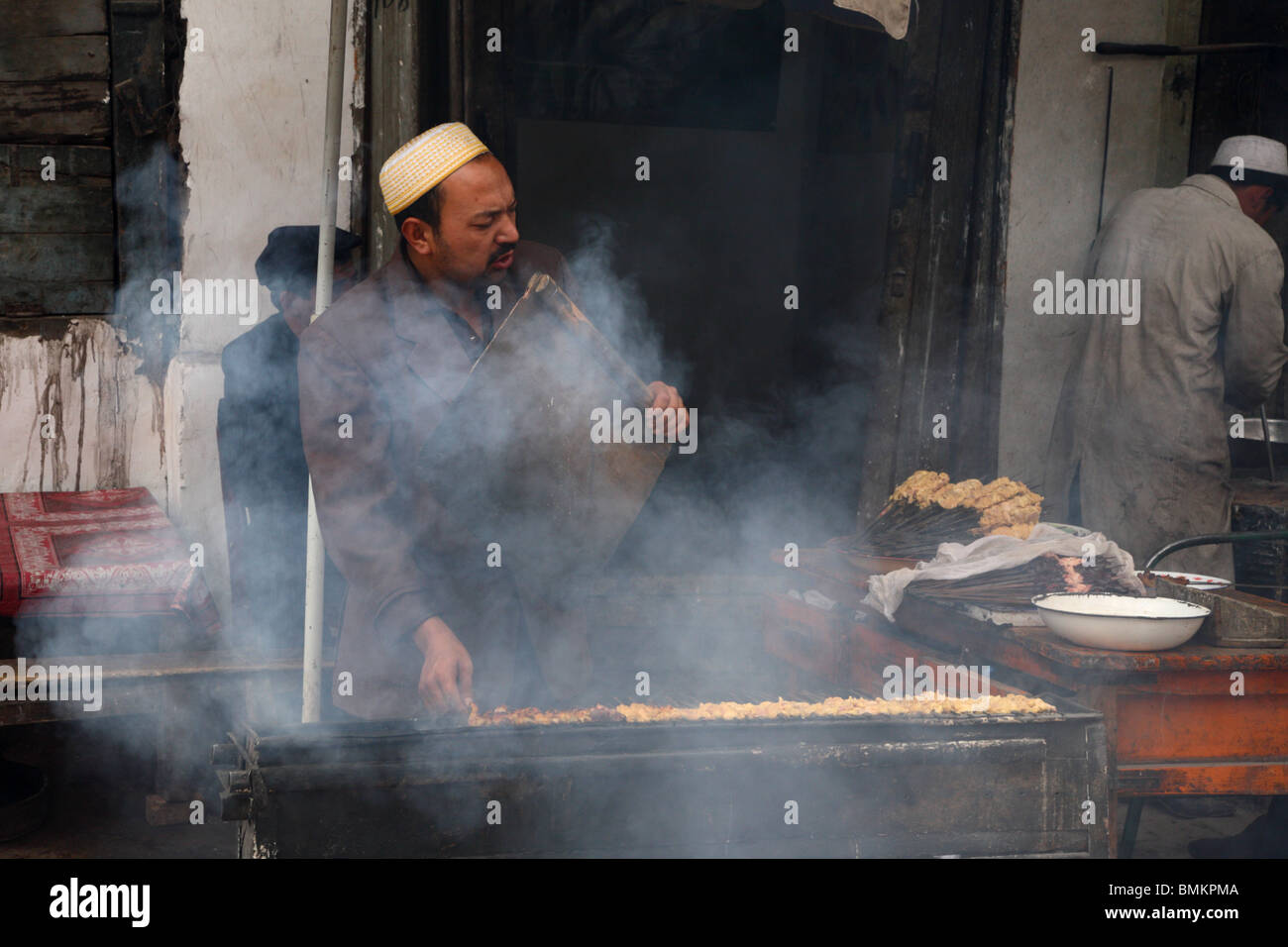 Lebensmittel Verkäufer schüren den Rauch, wie er in den Seitenstraßen von Kashgar im Westen von Xinjiang Provinz der VR China kocht. Stockfoto