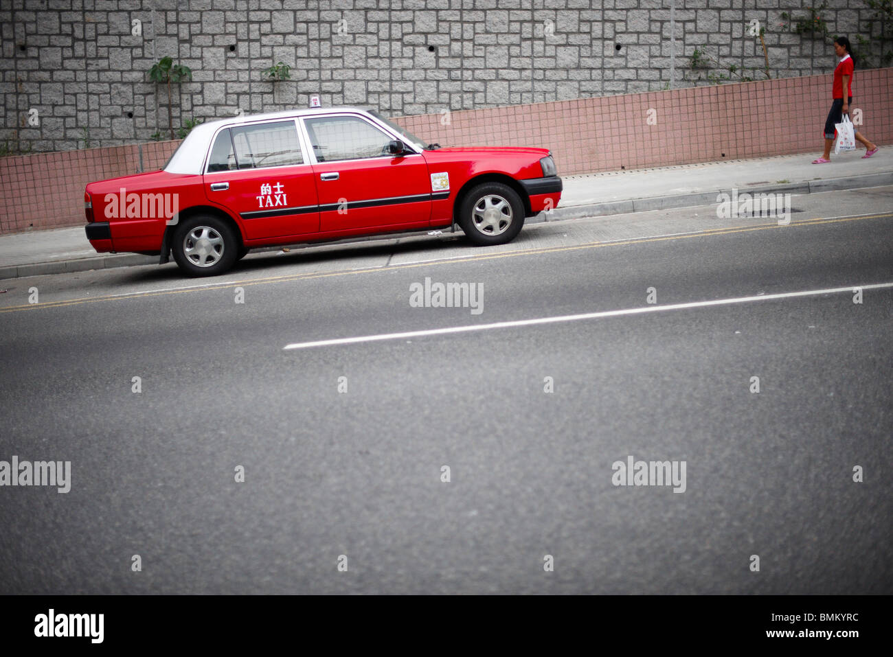Ein rotes Taxi parkte auf einem Hang mit einem Fußgänger Kleid in der gleichen auffällig rot zu Fuß in Richtung Auto, tragen weiße Plastiktüte. Stockfoto
