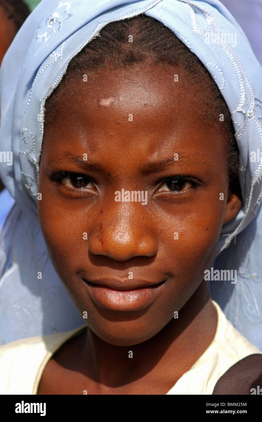 Niamey, Niger, Porträt von einem afrikanischen muslimische Schülerin mit einem blauen Schal für ihre Haare zaghaft lächelnd. Stockfoto