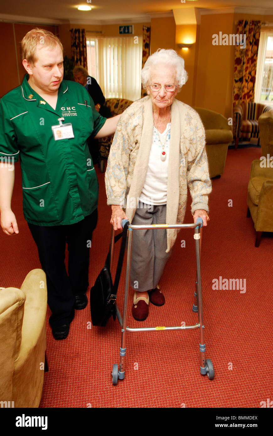 Healthcare Arbeitnehmer Unterstützung ein älterer Bewohner mit ihrer Mobilität in ein Altenheim, Wirral, Großbritannien. Stockfoto
