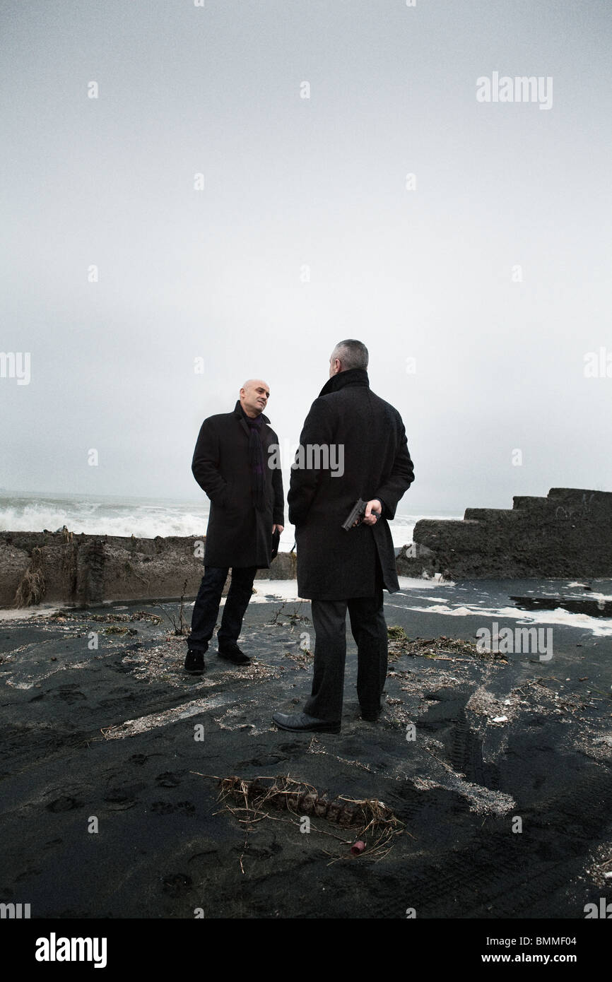 Zwei-Mann Gespräch am verlassenen Strand-One halten einer geladenen Waffe hinter seinem Rücken Stockfoto