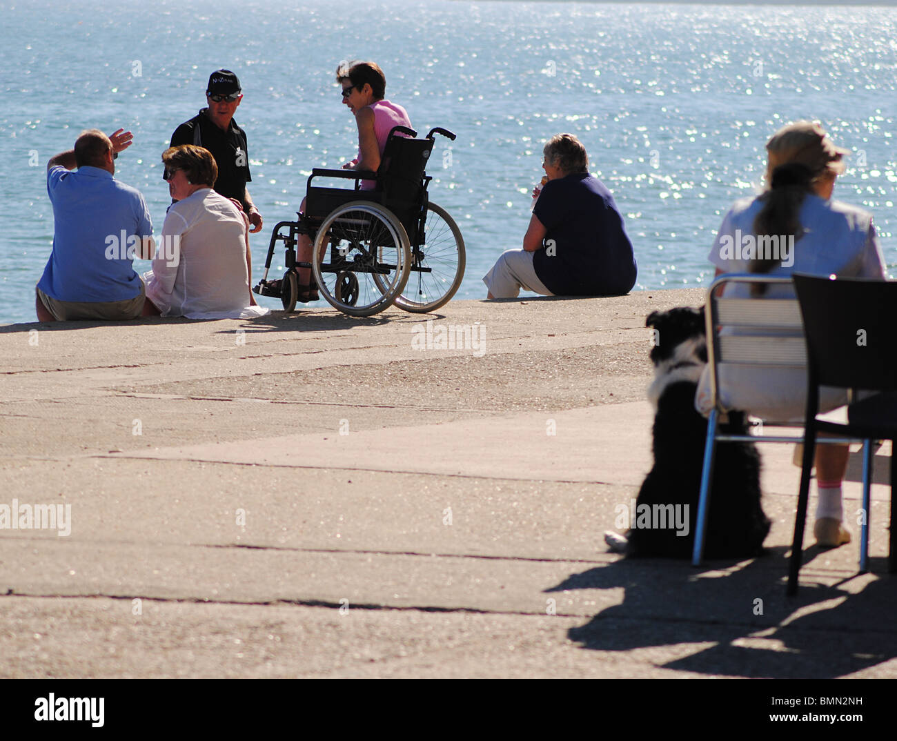Eine Frau in einem Rollstuhl spricht mit Freunden am Meer bei Charmouth, Jurassic Coast, Dorset, England Stockfoto