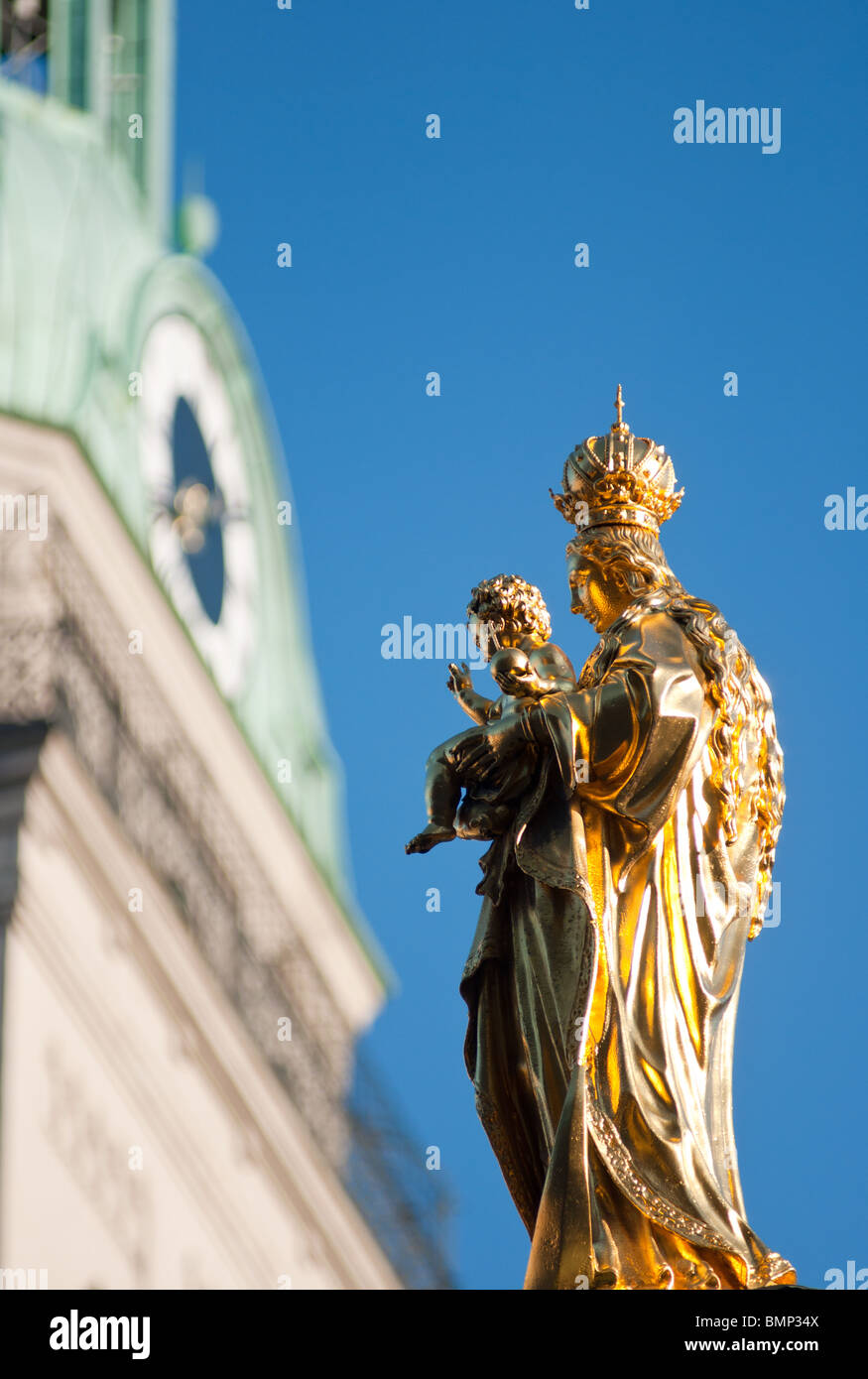 Goldene Statue der Maria mit dem Jesuskind am Marienplatz, mit der Peterskirche-Kirche im Hintergrund Stockfoto