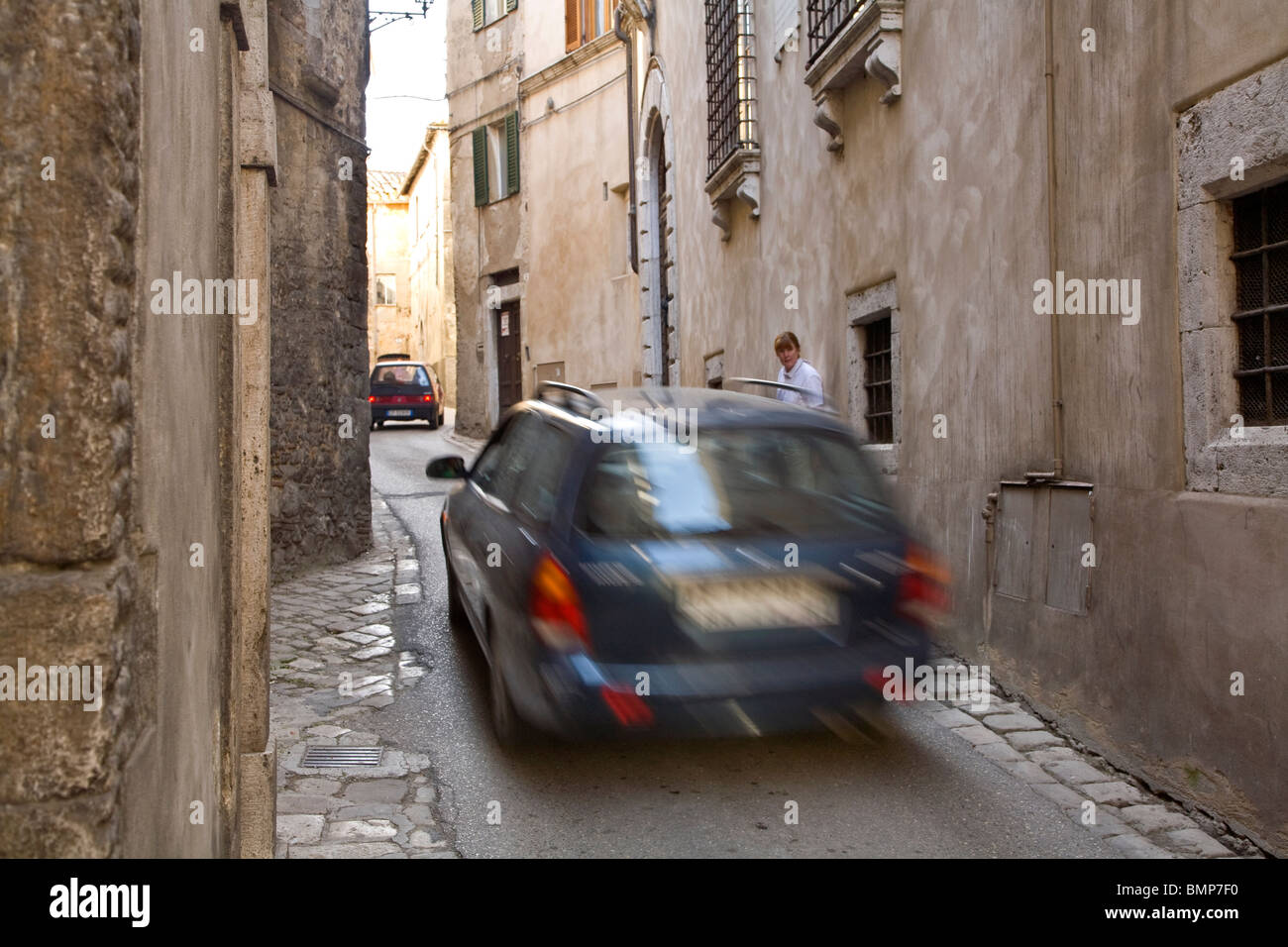 Fahrzeuge fahren während Fußgänger Uhren Verkehr Gebäuden, enge Gassen in der historischen Stadt von Amelia, Umbrien, Italien Stockfoto