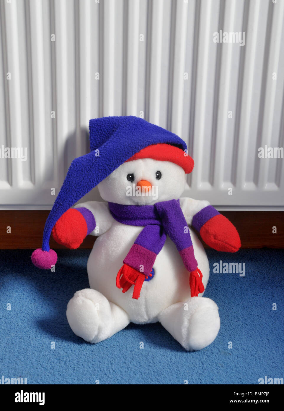 ein weiches Plüschtier Schneemann mit einem Hut und Schal sitzt auf dem Teppich an den Heizkörper gelehnt. Stockfoto