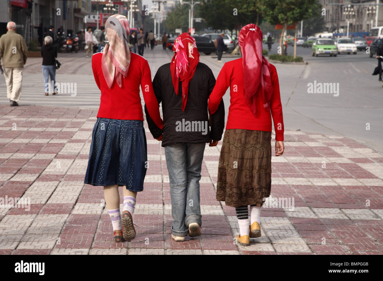 Drei junge Frauen gehen Arm in Arm in den Straßen von Kashgar, westliche Xinjiang-Provinz, China. Stockfoto