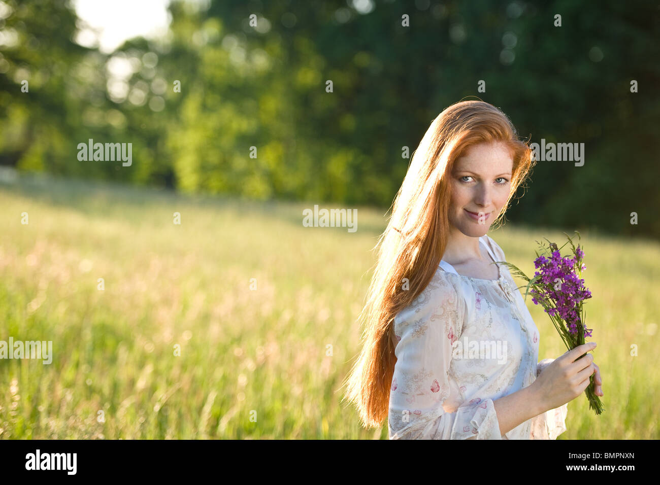 Langes rotes Haar Frau im romantischen Sonnenuntergang Wiese mit Blumenstrauß Stockfoto