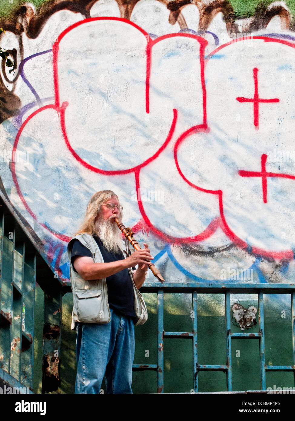 Gegenübergestellt mit einer großen Bande Grafitti, spielt bärtiger Straßenmusiker seine Querflöte in New Yorks Lower East Side. Stockfoto