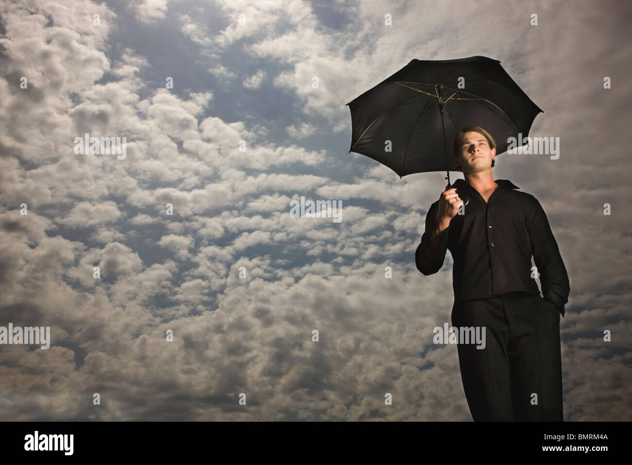 Ein Mann hält einen Regenschirm unter einem Himmel voller Wolken Stockfoto