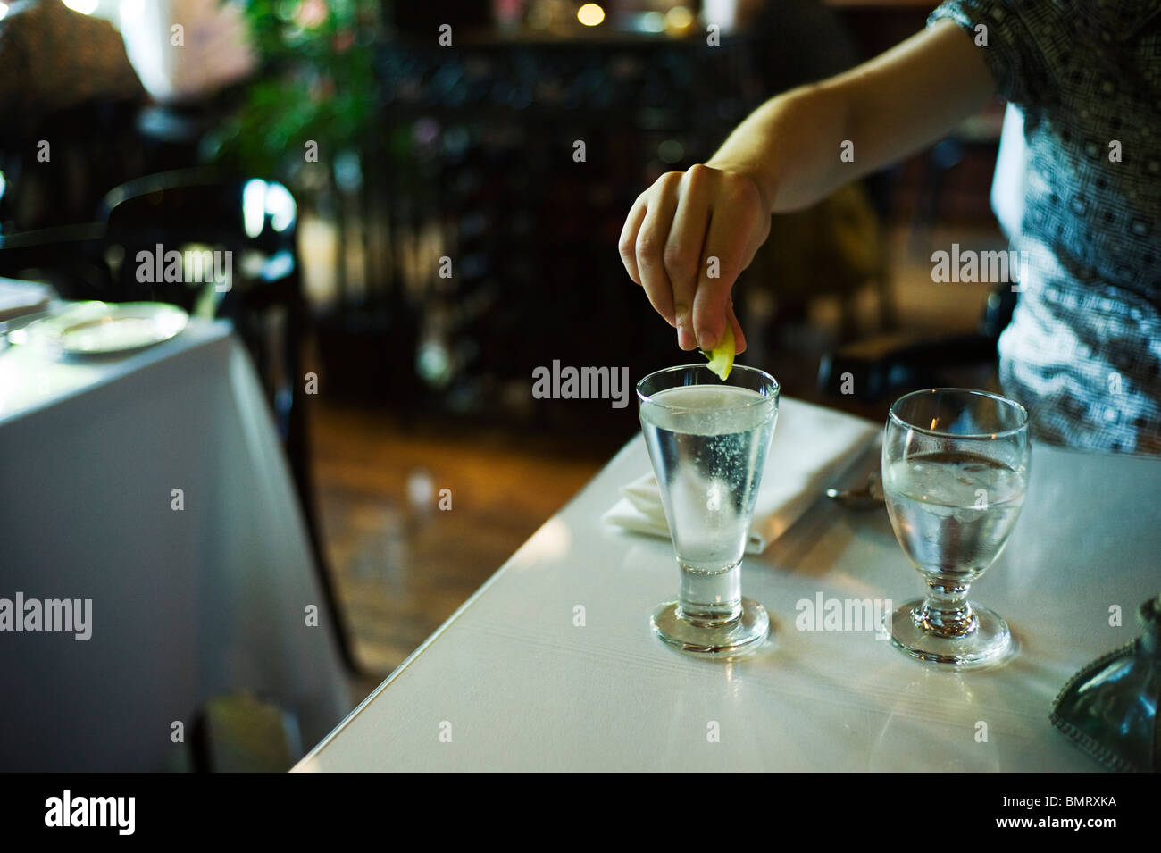 Arm und die Hand der Frau als sie Scheibe Zitrone in ein Glas Wasser mit Kohlensäure drückt. Stockfoto