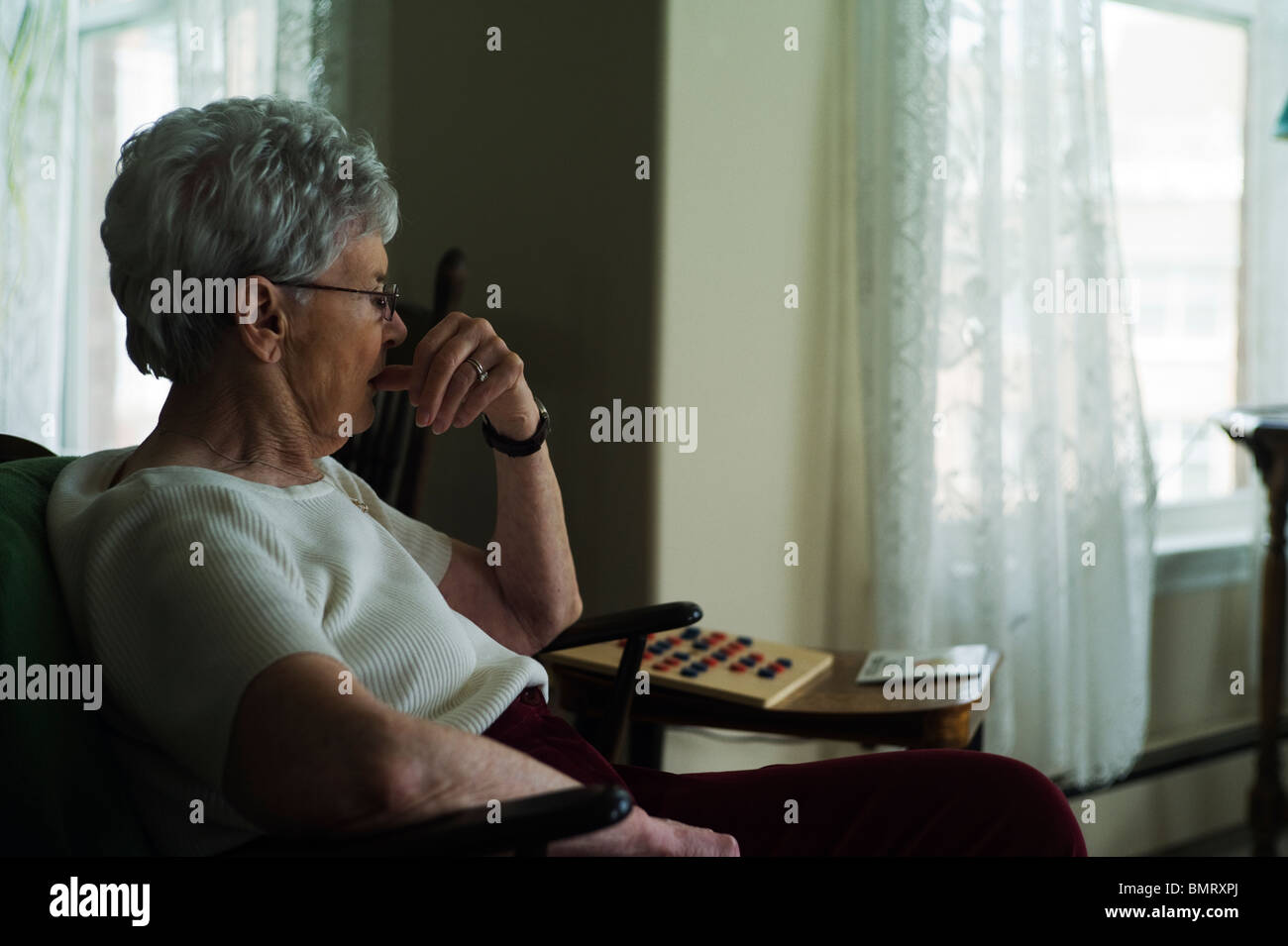 Alte Frau sitzt im Wohnzimmer Stuhl, Fingernägel kauen. Stockfoto