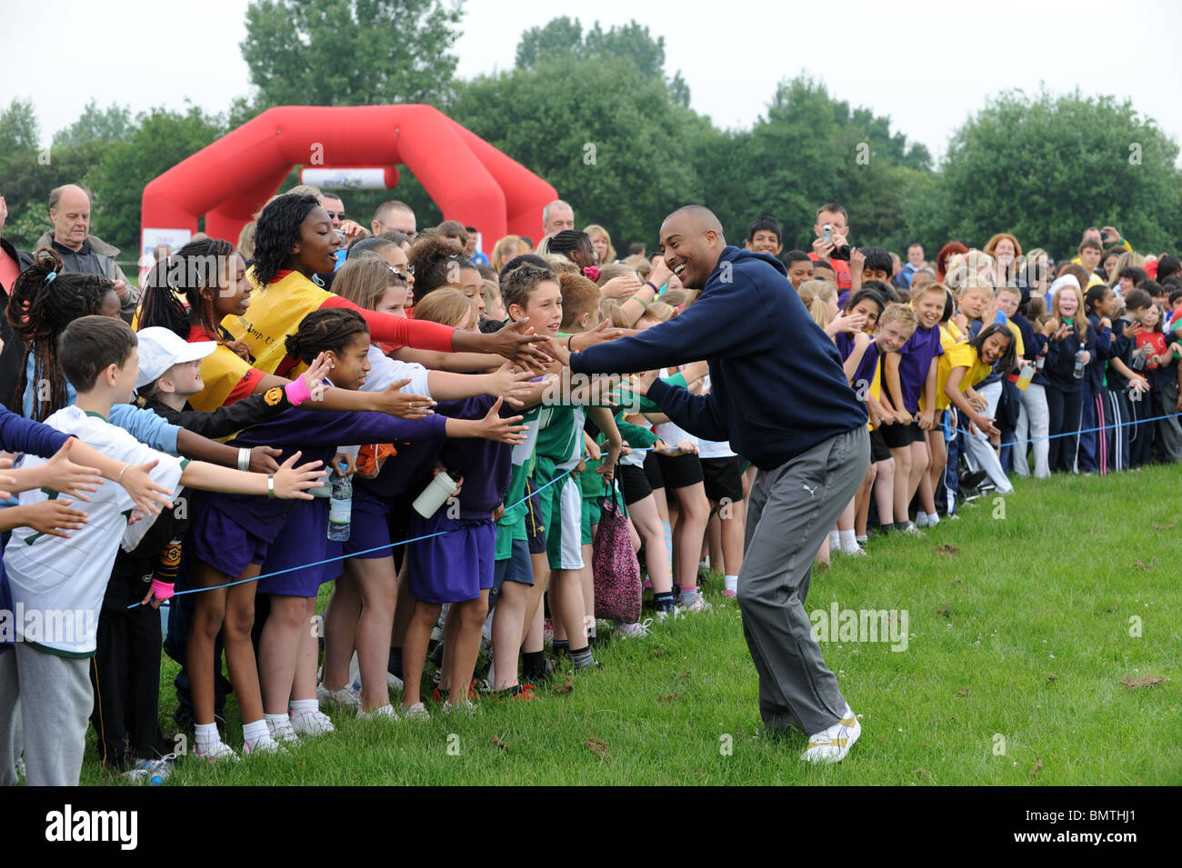 Colin Jackson tut eine Ohrfeige Hände schütteln mit Hunderten von Kindern, die Teilnahme an der Tesco große Schule laufen Stockfoto