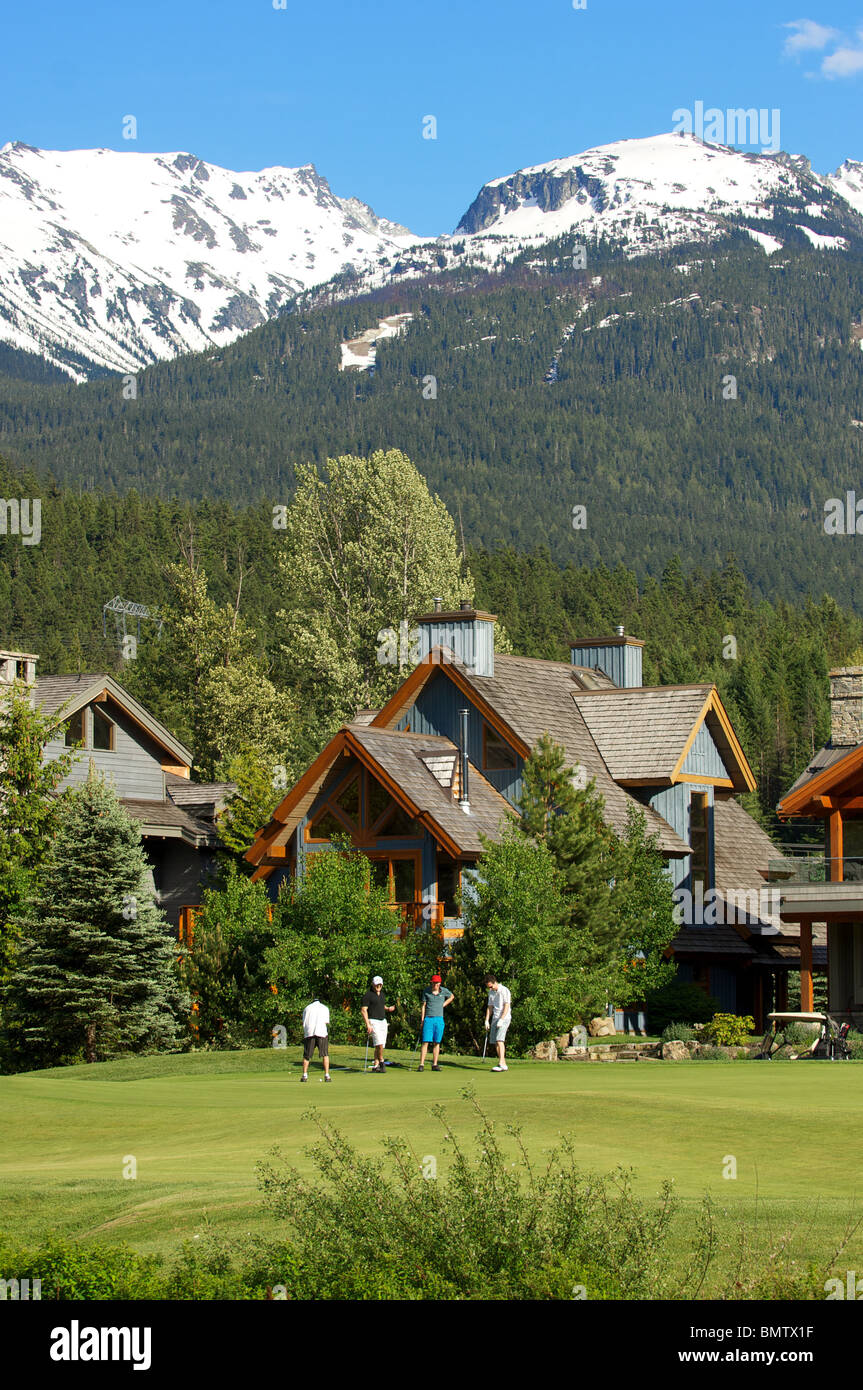 Eine Gruppe von Golfern spielen Sie eine Runde im Nicklaus North Golf Club unter einem verschneiten Berggipfel. Whistler, BC, Kanada Stockfoto