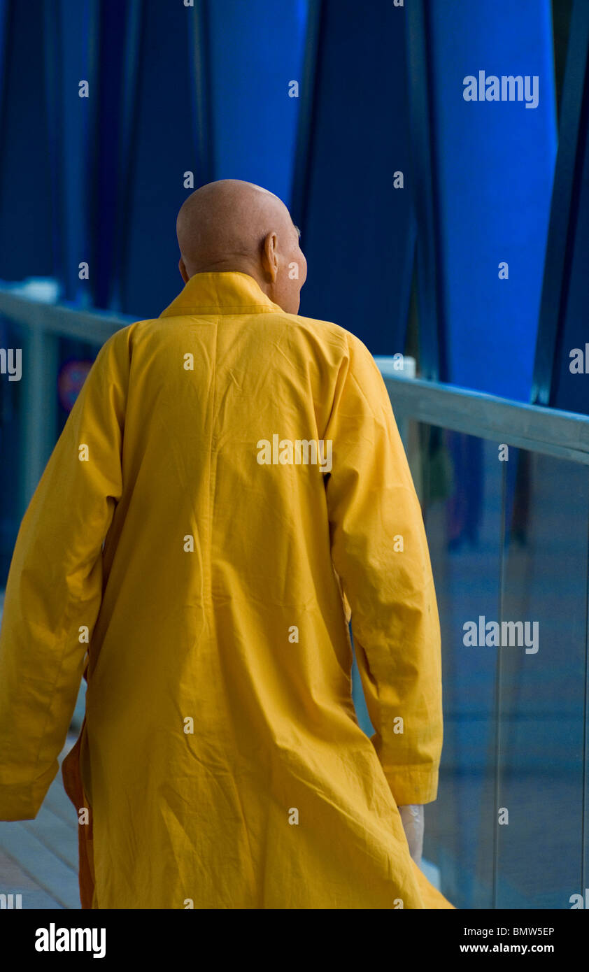 Ein buddhistischer Mönch in einem hellen gelben Regenmantel Spaziergänge entlang der Küste in der Nähe der Star Ferry in Hong Kong Central District. Stockfoto