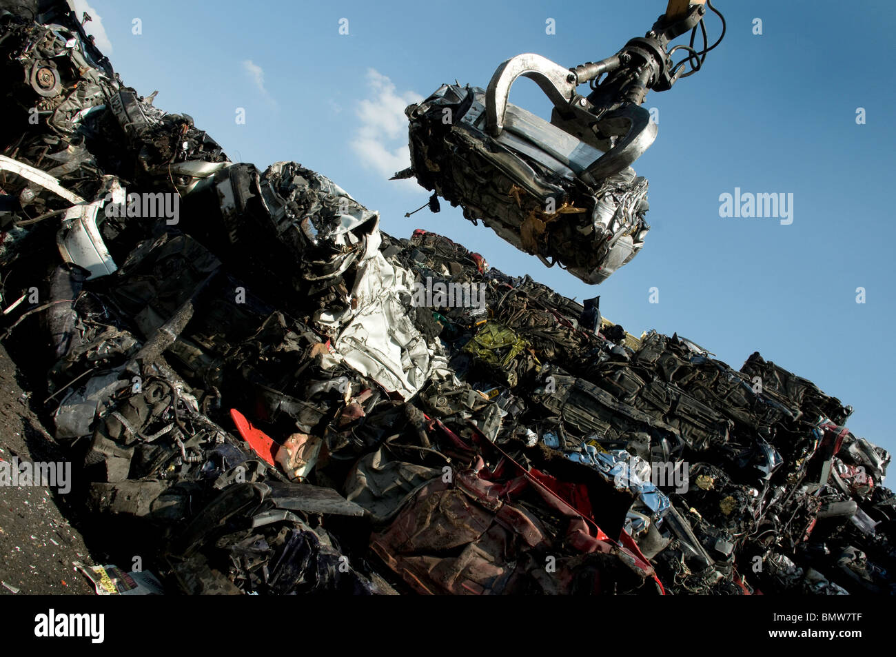 Hof-Kran mit zerdrückten Auto mit anderen zerkleinerten verschrotteten Autos in Haufen Schrott. Stockfoto