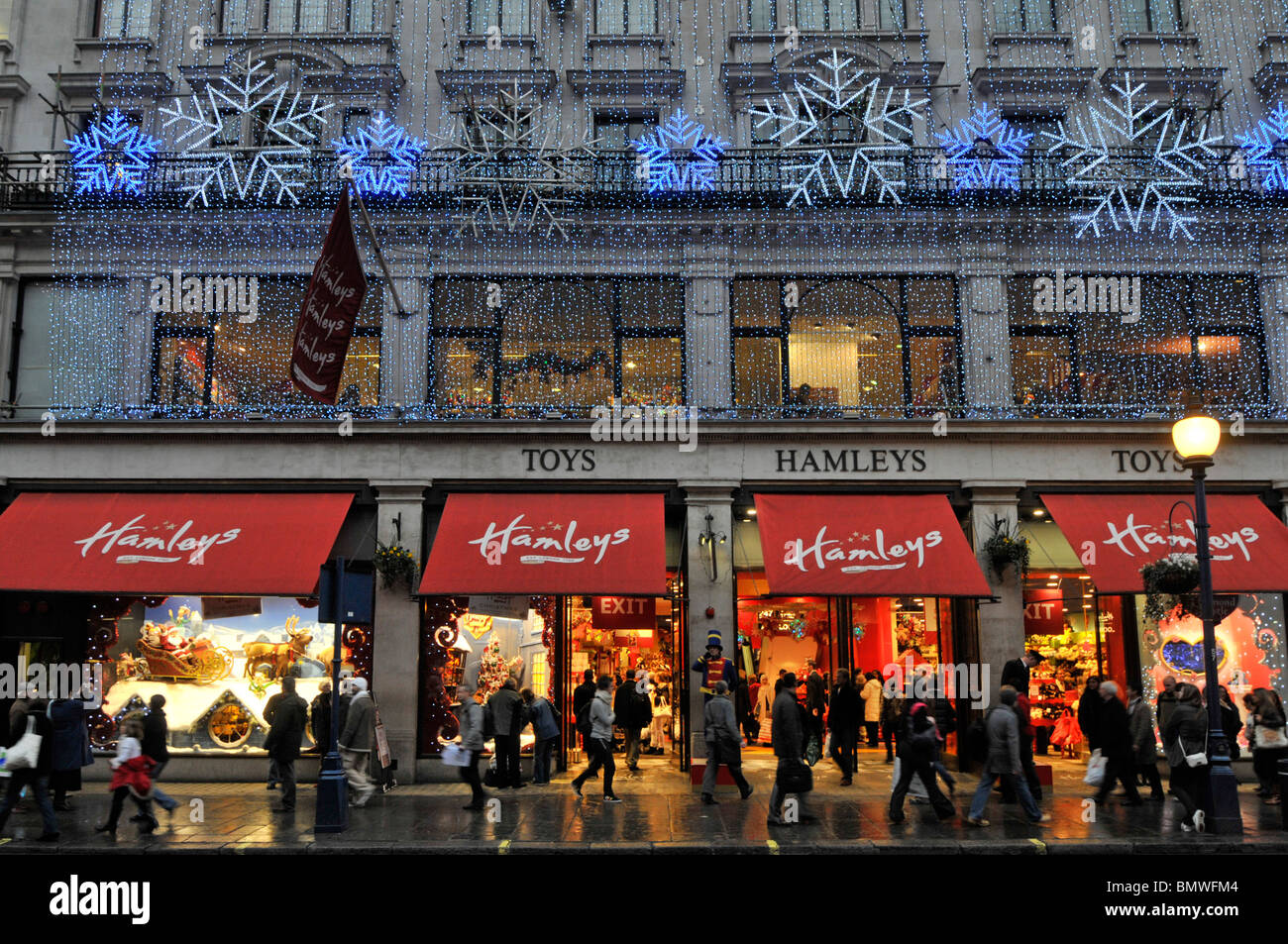 Hamleys Spielzeugladen Laden Markenlogo auf Fensterläden Winter Abenddämmerung beschäftigt mit Weihnachtseinkäufern in Regent Street West End Weihnachtsbeleuchtung Dekorationen London UK Stockfoto