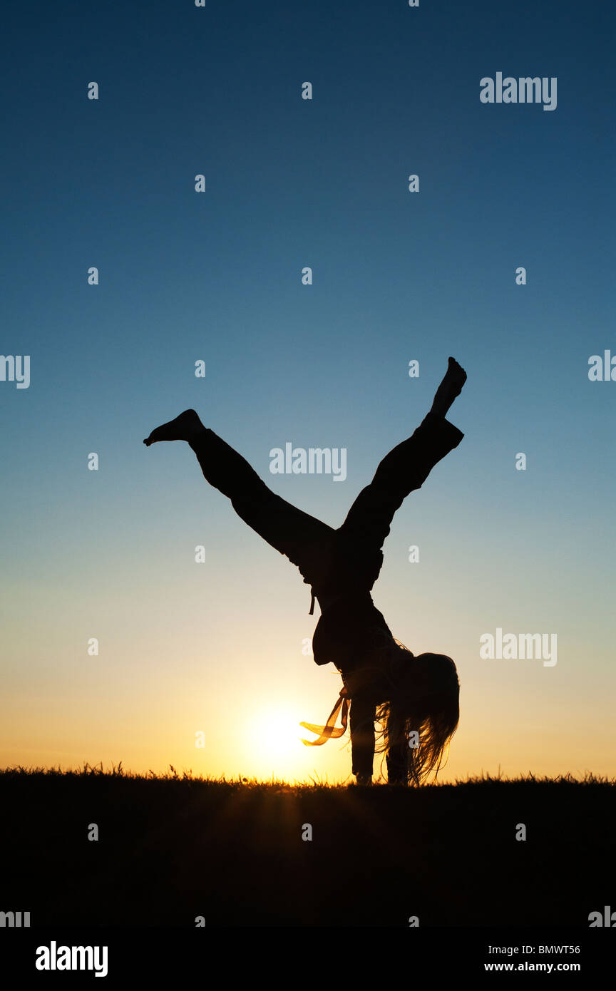 Young Girl energetisch Spaß macht einen Handstand bei Sonnenuntergang. Silhouette Stockfoto