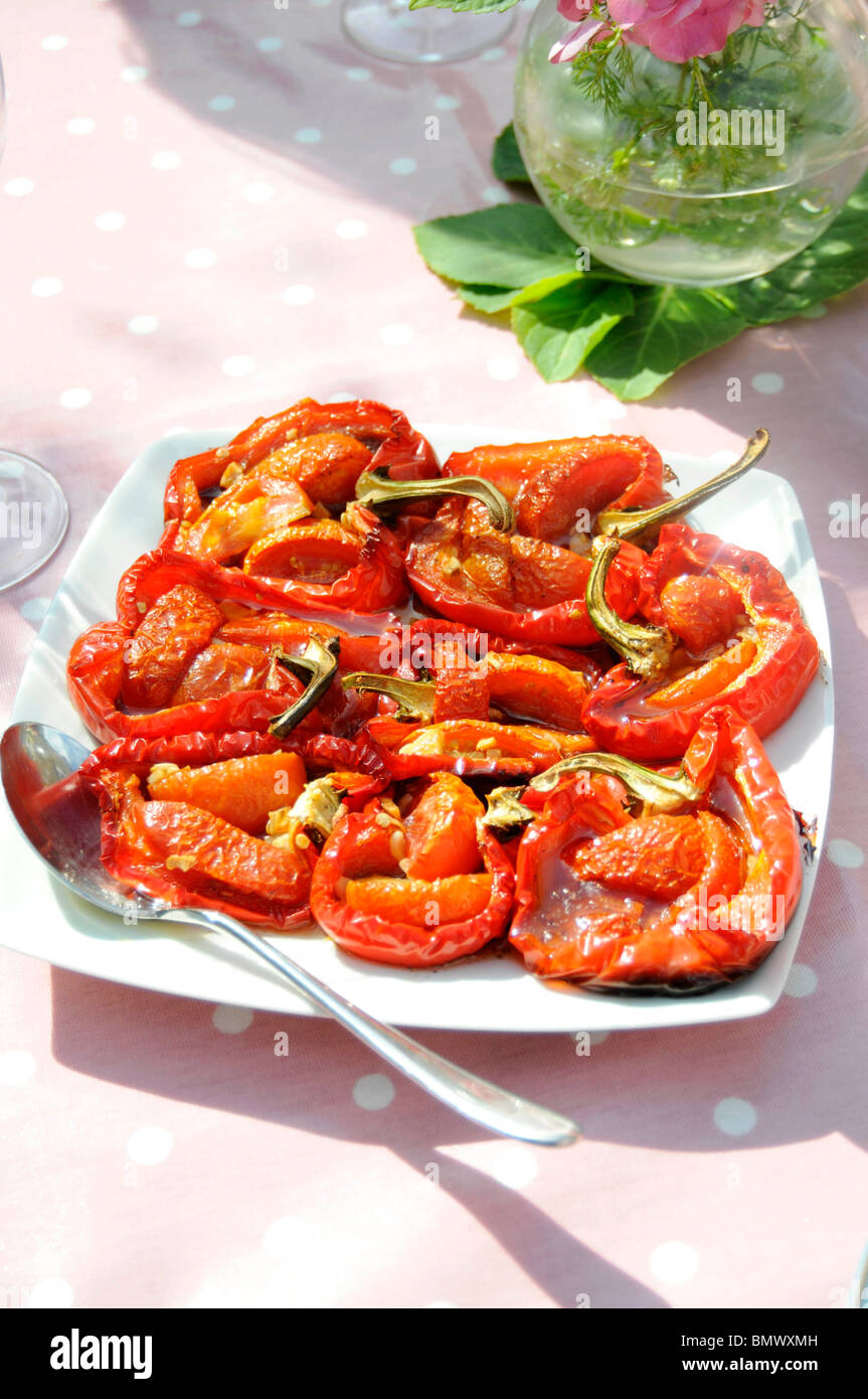 Geröstete Paprika mit Tomaten und Knoblauch auf einem weißen Teller auf rosa Tischdecke Stockfoto