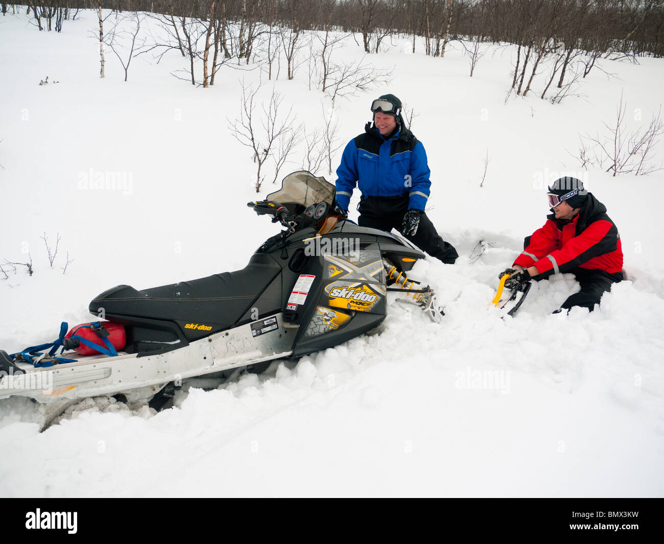 Zwei Männer, 25 und 45 Jahre alt, ziehen Sie eine festgefahrene Schnee mobile aus den Tiefschnee. Stockfoto