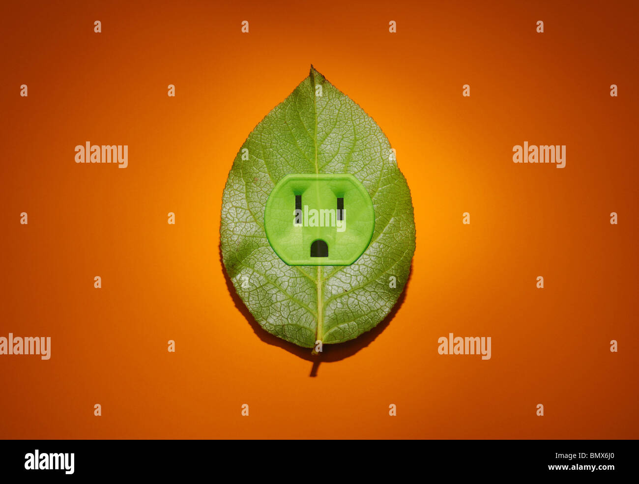 Eine grüne Pflanze Blatt mit elektrischer Energie Outlet, orange Hintergrund Stockfoto