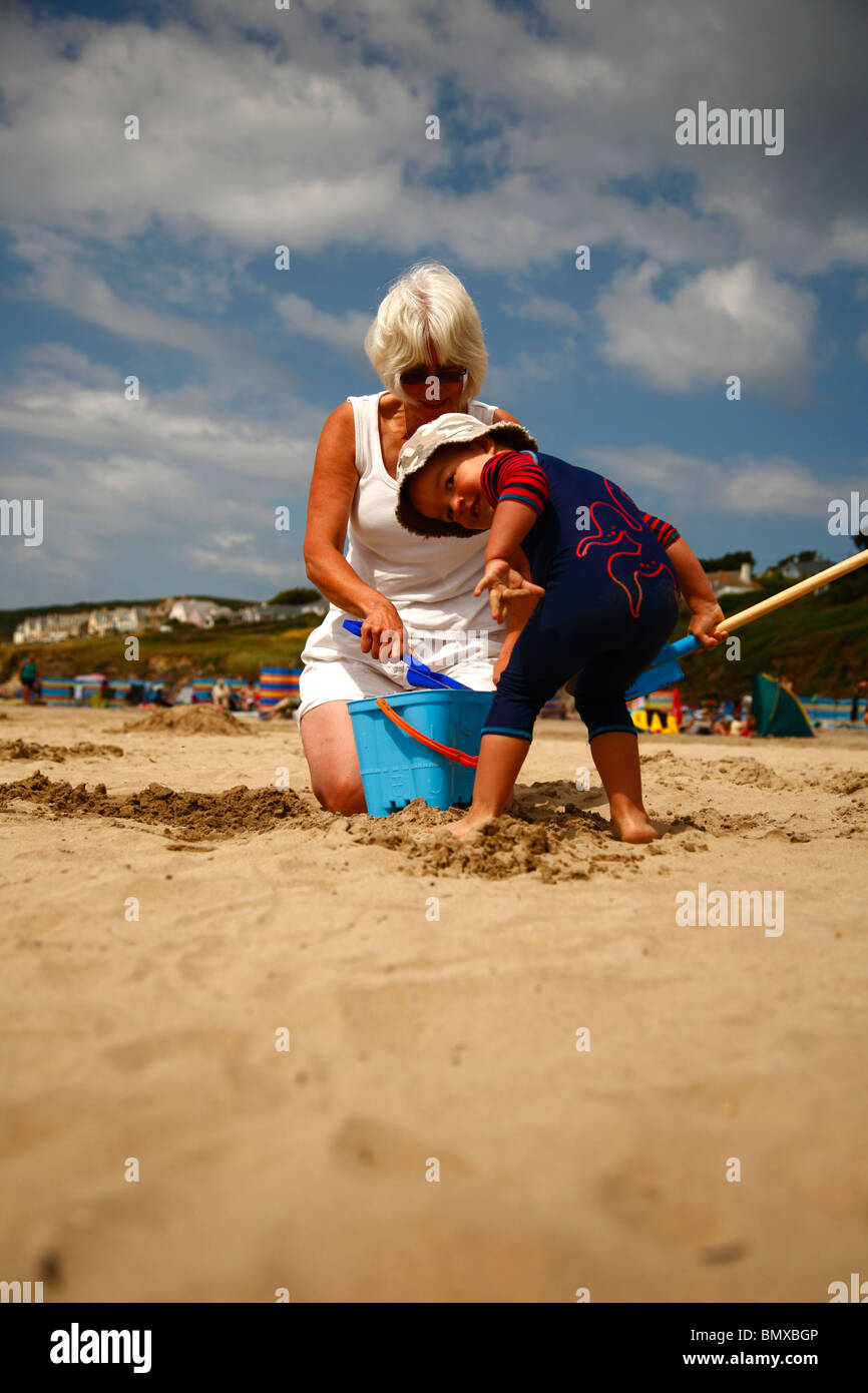 Ein kleiner Junge, der Spaß am Strand mit seiner Großmutter und einem Eimer und Schaufel in Polzeath, Cornwall zusammen zu spielen. Stockfoto