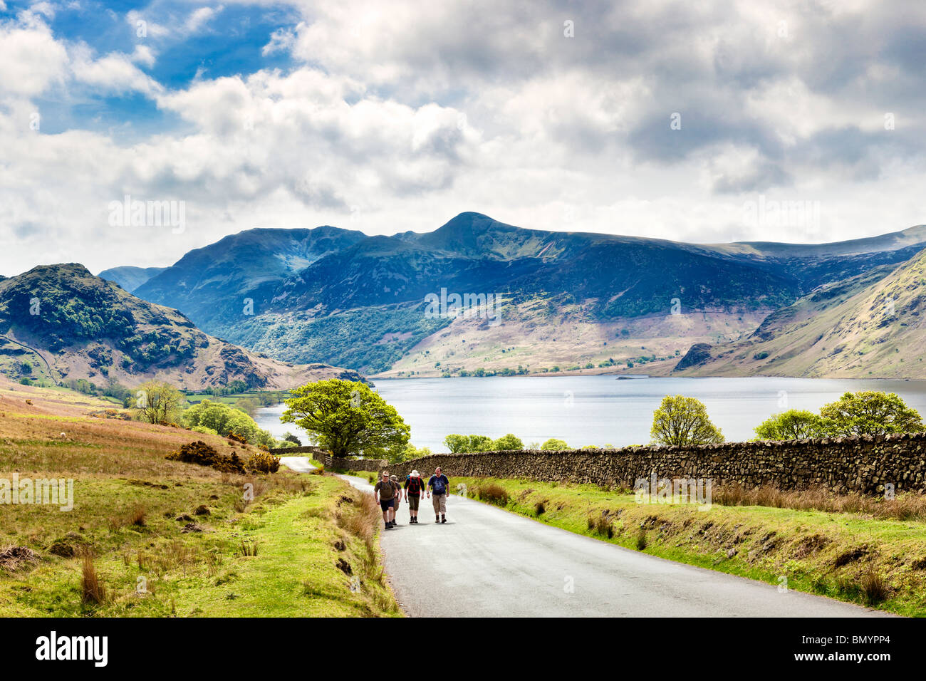 Wanderer zu Fuß auf der Straße vorbei an Crummock Wasser, Lake District, England, UK mit hohem Stil und rot Hecht Bergen im Frühjahr Stockfoto