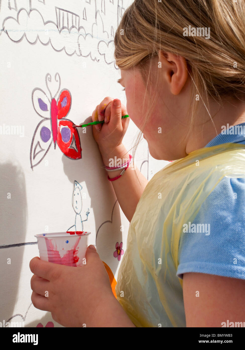 Sieben Jahre alte Blondine Malerei eines Schmetterlings auf ein Wandbild an der Wand Stockfoto