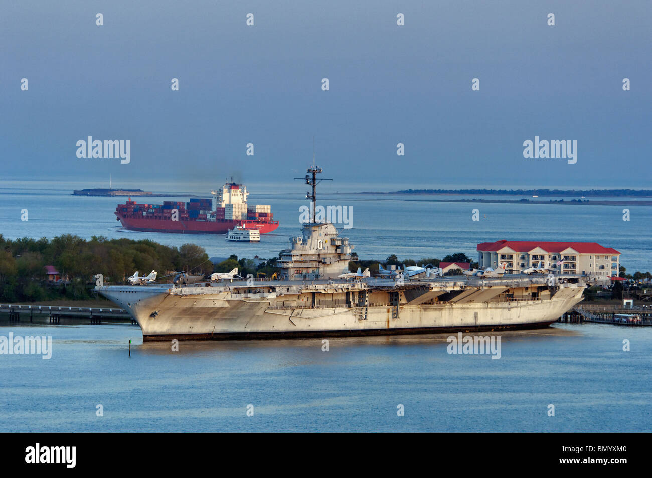 Containerschiff vorbei an der USS Yorktown in der Abenddämmerung mit Fort Sumter in der Ferne in der Nähe von Charleston, South Carolina Stockfoto