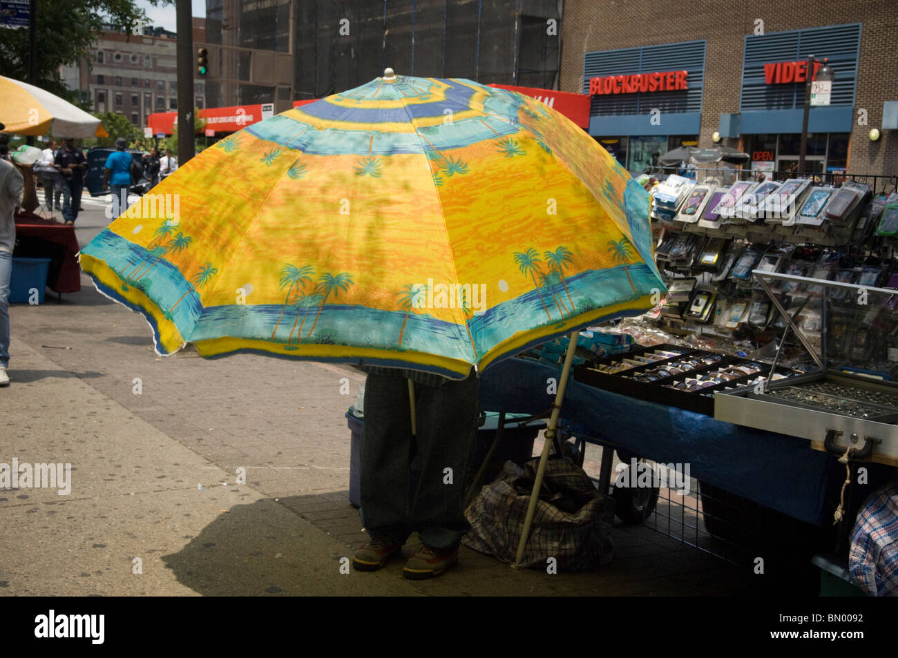Eine Straße Verkäufer unter einem riesigen Dach an einem sonnigen Tag an der 125th Street im Stadtteil Harlem in New York Stockfoto