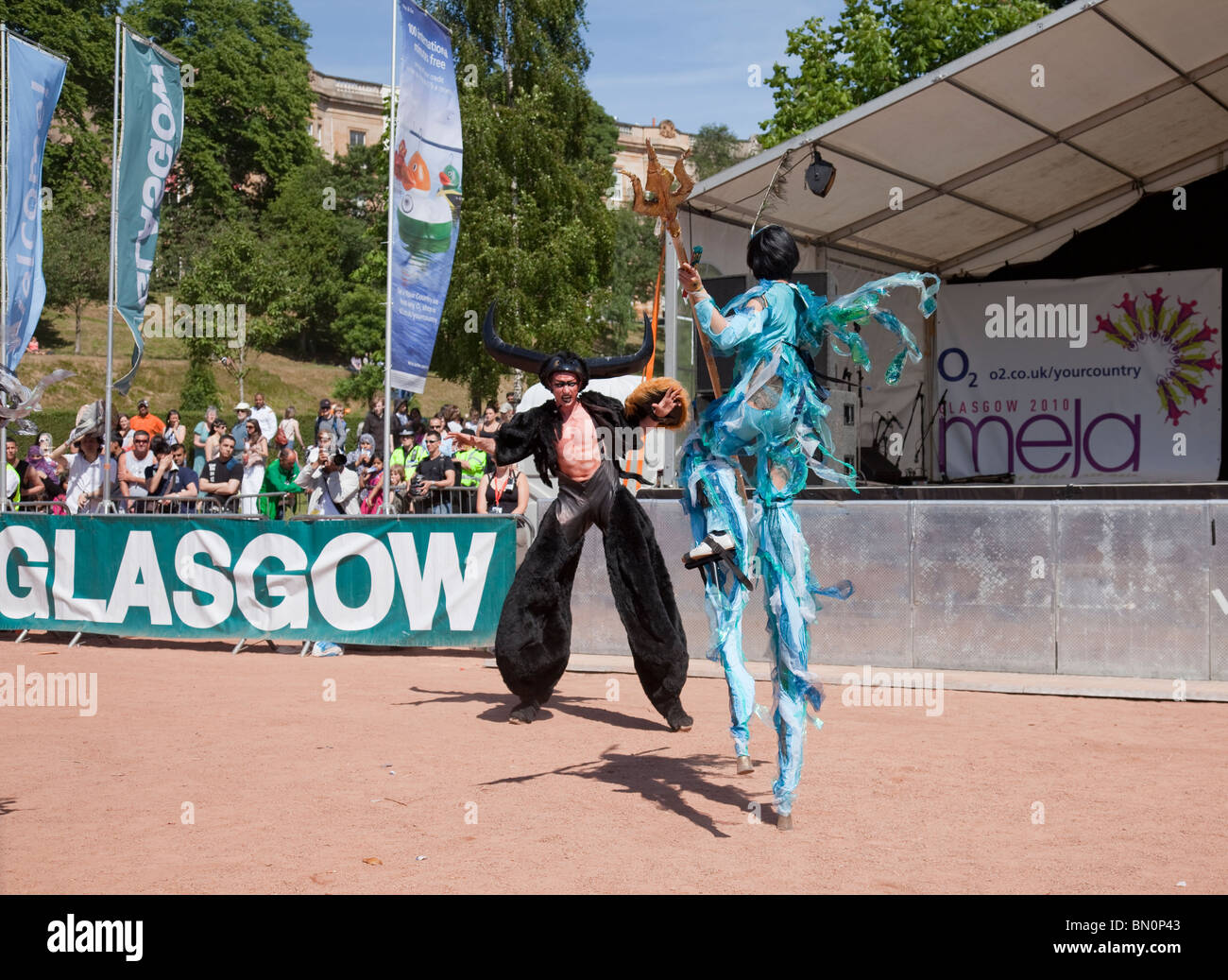 Akteure auf Stelzen, ein Pfau und Mahisha, ein Wasser-Buffalo-Daemon aus der hinduistischen Mythologie, Natur für Symbole in Glasgow Mela 2010 Stockfoto