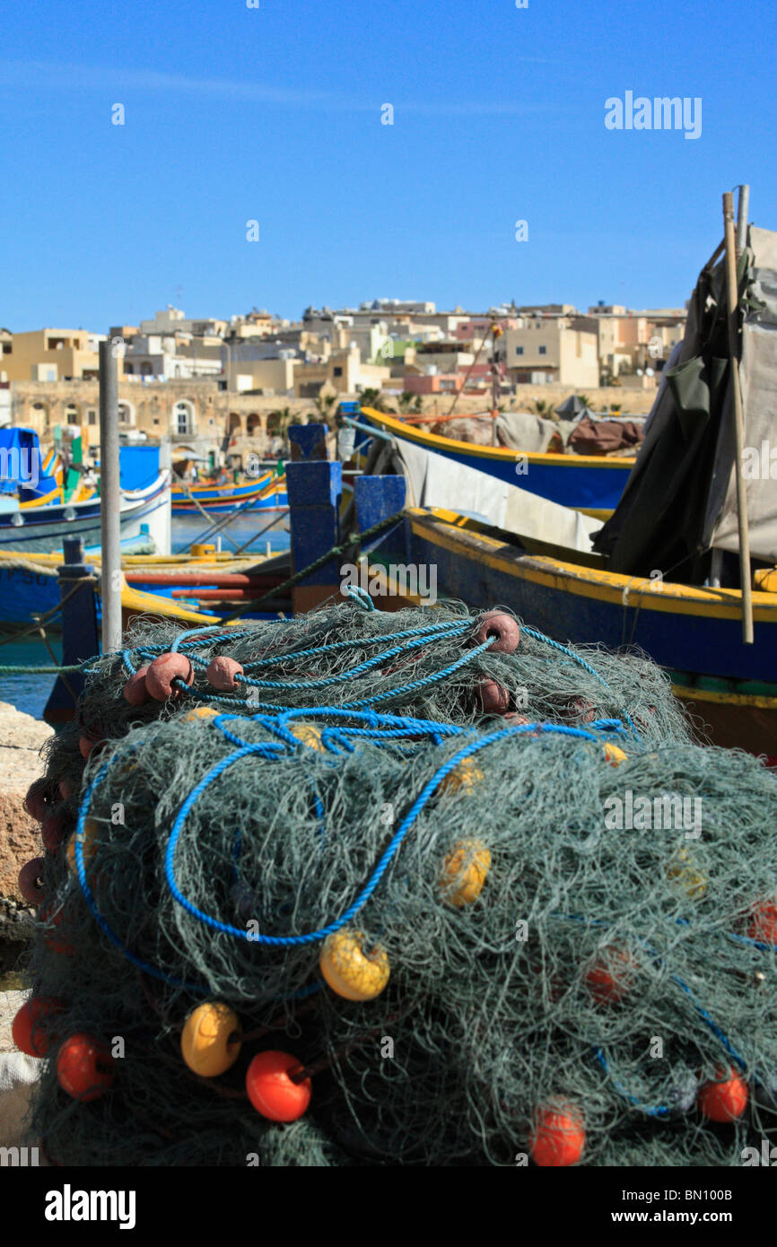 Gerollt, Fischernetze im Vordergrund einer Hafen-Szene in Marsaxlokk, Malta, mit bunten Booten oder luzzu Stockfoto