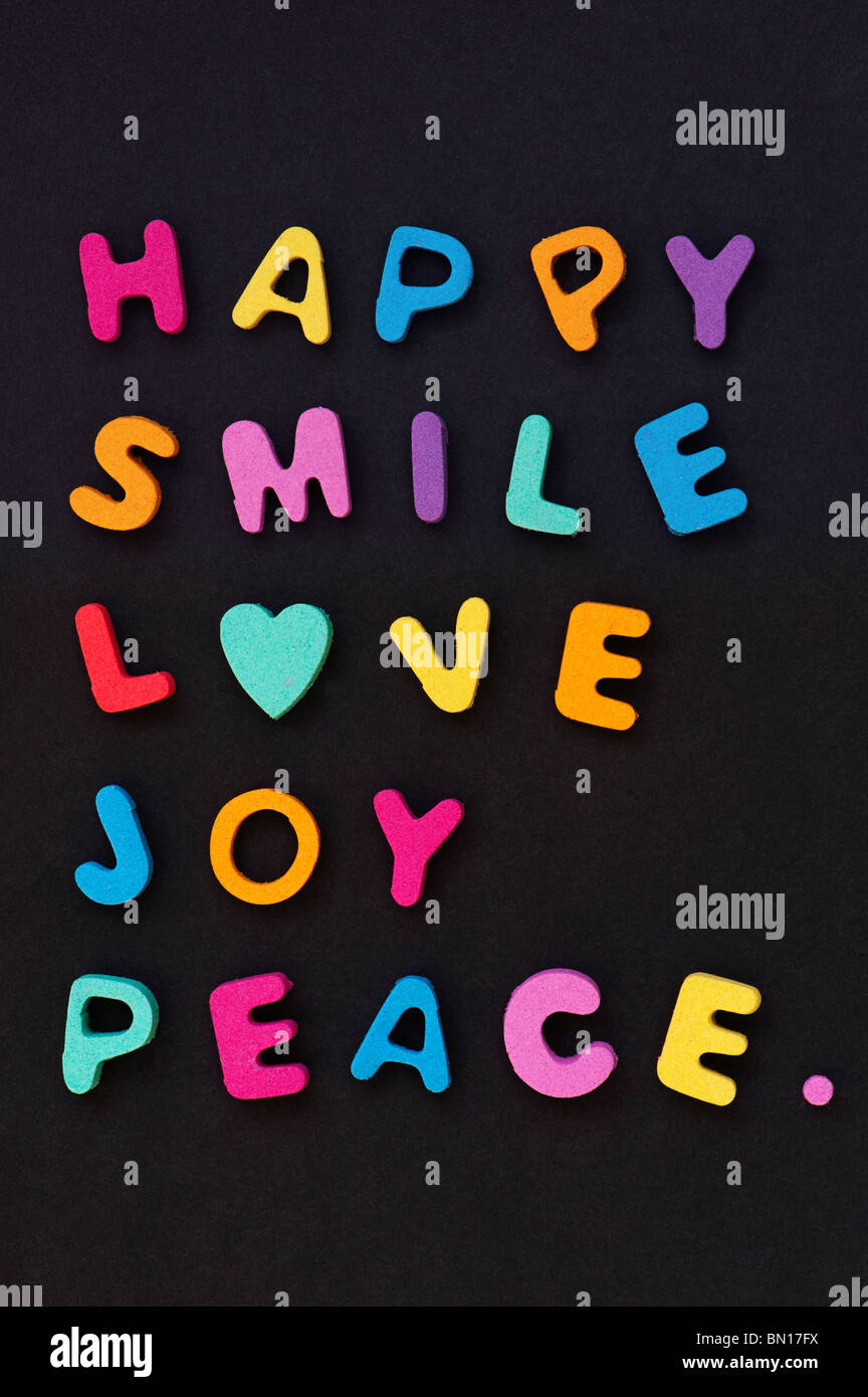 Bunte Worte Liebe Lächeln glücklich Freude und Frieden mit der Form eines Herzens auf schwarzem Hintergrund Stockfoto