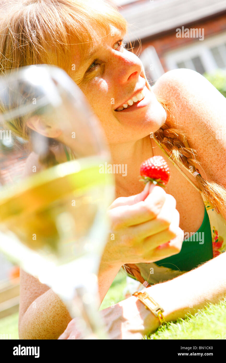 Frau in ihren Dreißigern Erdbeeren in ihrem Garten essen und trinken ein Glas Wein Stockfoto