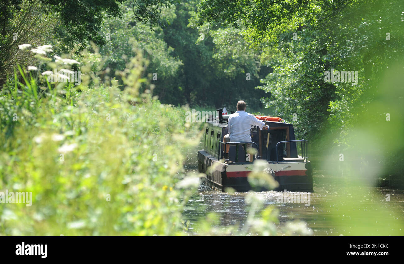 EIN MANN STEUERT EINE NARROWBOAT BARGE AN EINEM BRITISCHEN KANAL WIEDER FERIEN FREIZEIT RUHESTAND ENTSPANNUNG WASSERSTRAßEN FREIZEITBESCHÄFTIGUNGEN HOBBYS UK Stockfoto