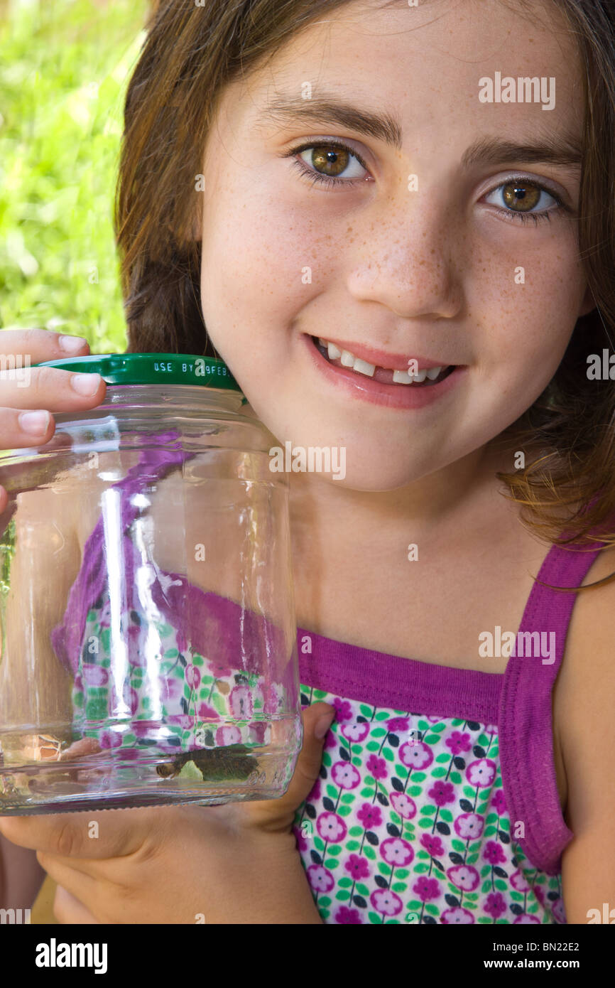 Kaukasische Mädchen hält ein Glas mit einer Raupe, die sie gefangen genommen hat.  Sie lächelt und ist sehr stolz auf sich selbst. Stockfoto