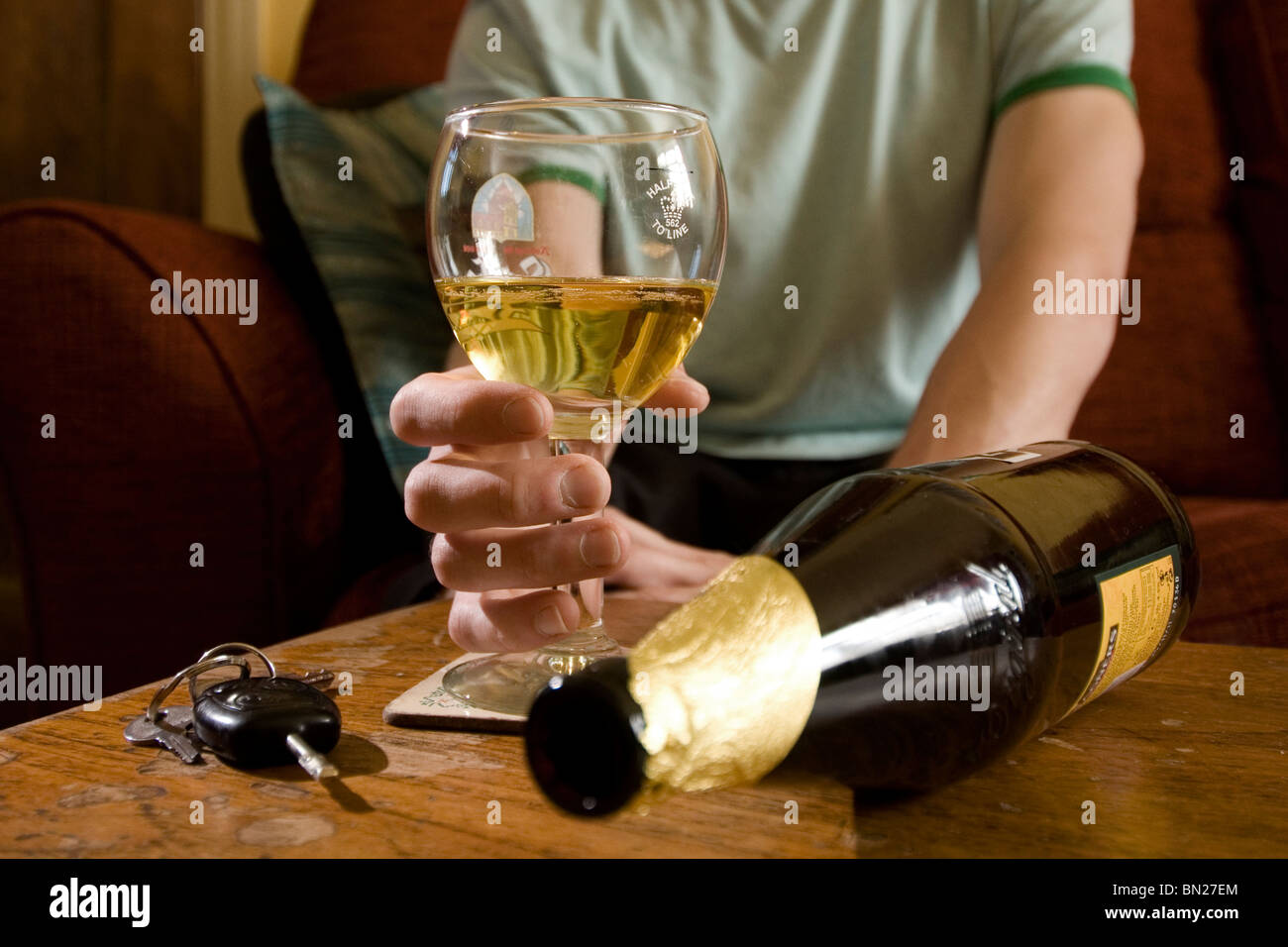 Ein Glas Bier in der einen Hand Personen neben einer Reihe von Autoschlüssel und eine leere Flasche auf seiner Seite unscharf Stockfoto