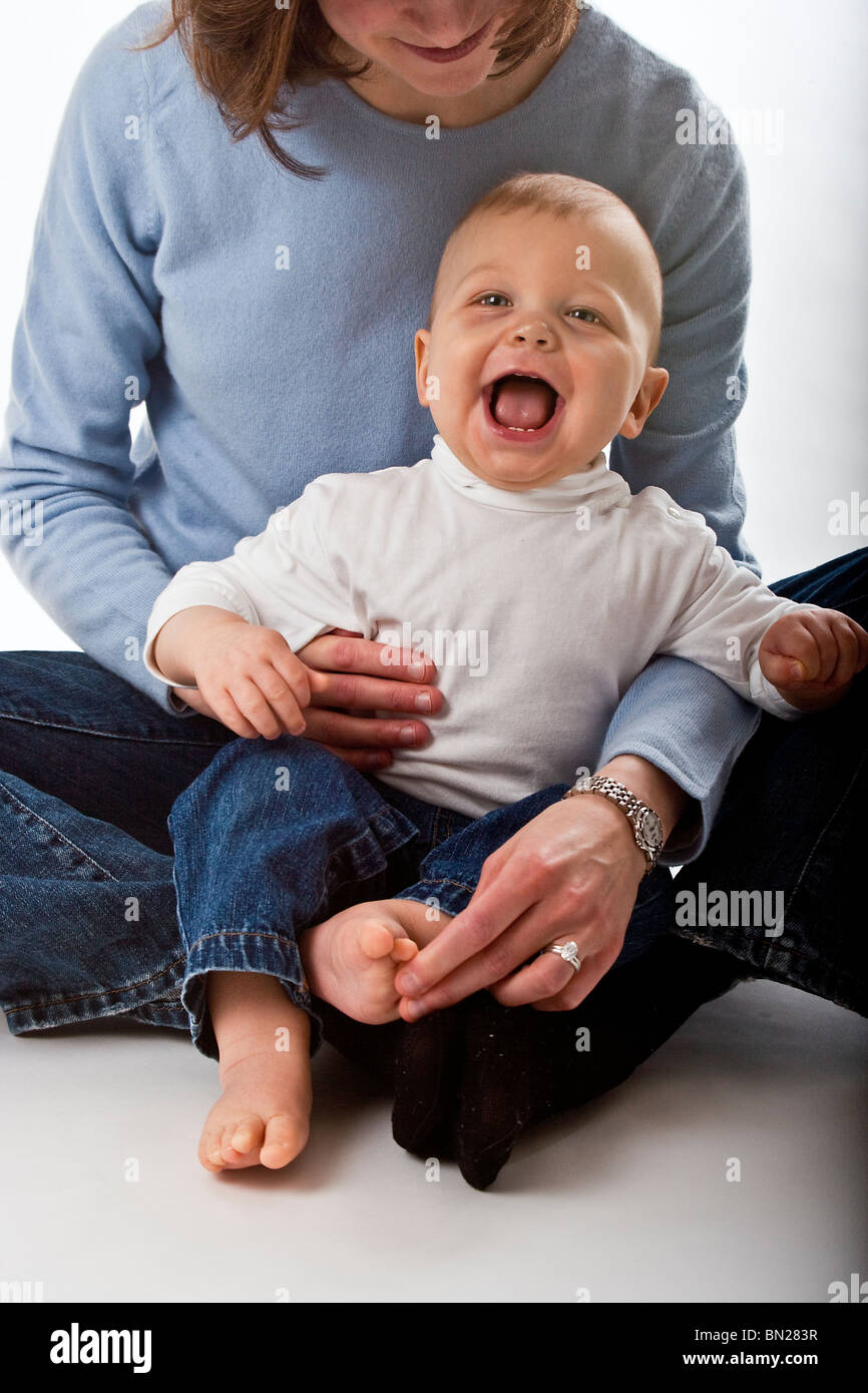 Kaukasische Babyjungen sitzt in seiner Mutter Schoß. Er lacht, weil sie seinen Fuß kitzeln ist. Stockfoto