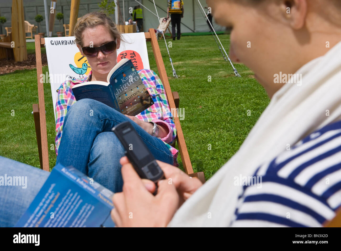 Junge Frauen, die Bücher lesen und SMS saß in Liegestühlen in der Sonne bei Hay Festival 2010 Hay on Wye Powys Wales UK Stockfoto