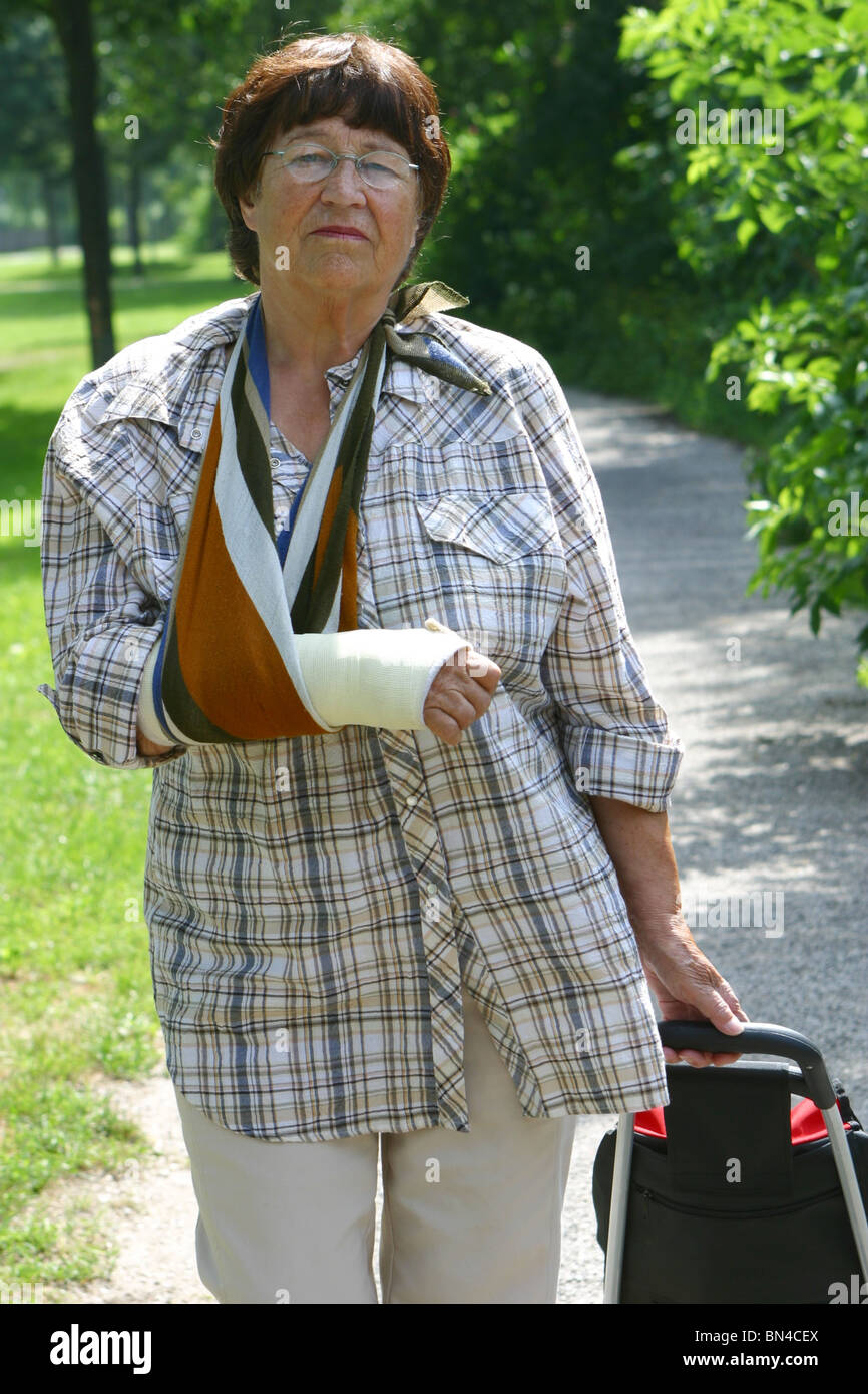 Ältere Frau macht einen Spaziergang in den Park mit Darsteller Arm in der Schlinge und gebrochenen arm Stockfoto