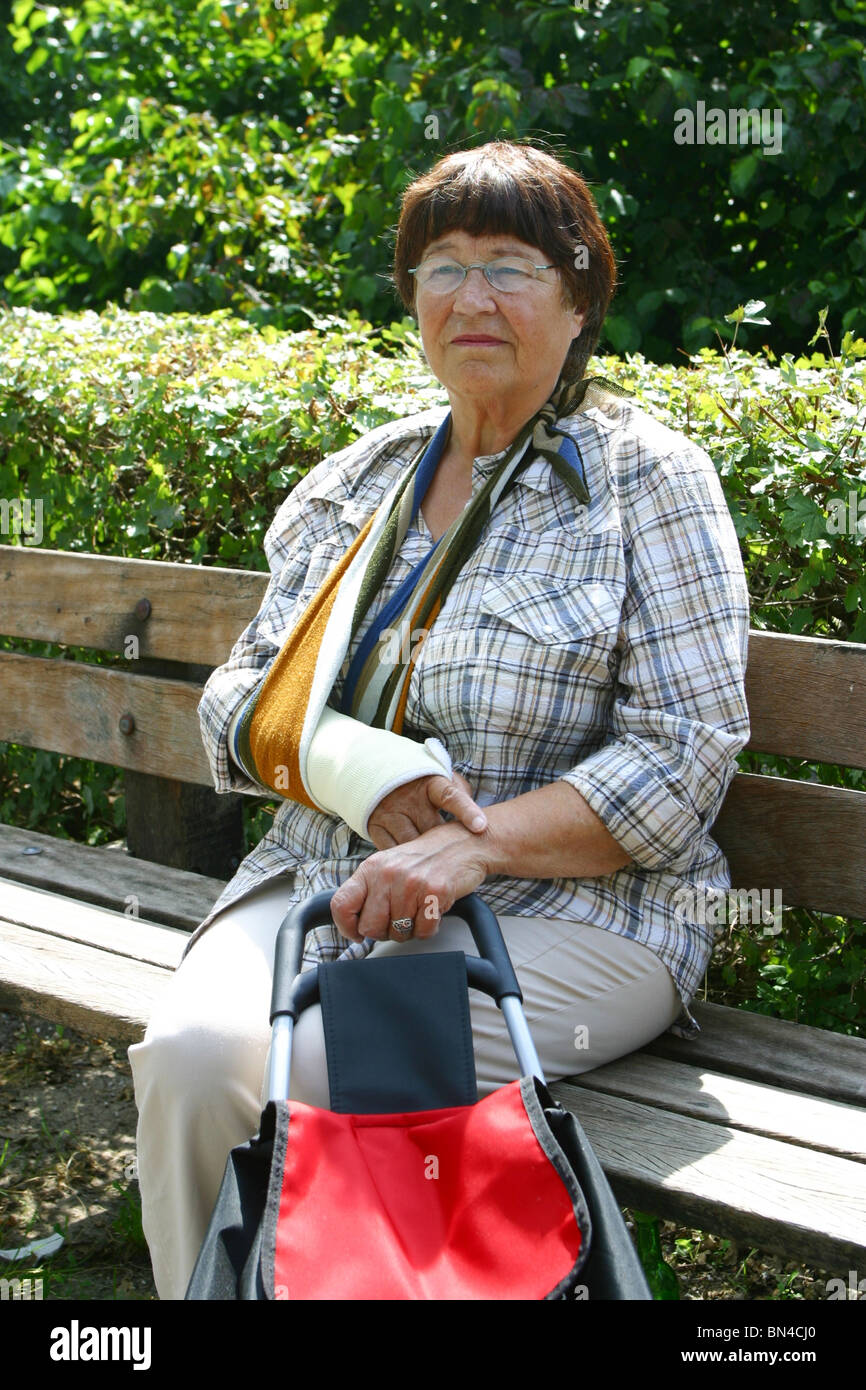 Rentner Frau mit Arm in der Schlinge auf Parkbank auf Parkbank Stockfoto