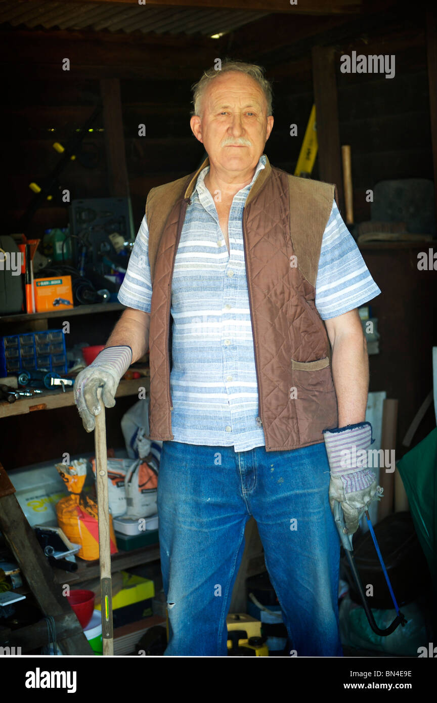 grauen Haaren ältere Landwirt steht in seinem Stall mit Handschuhen, starrte auf die Kamera Stockfoto
