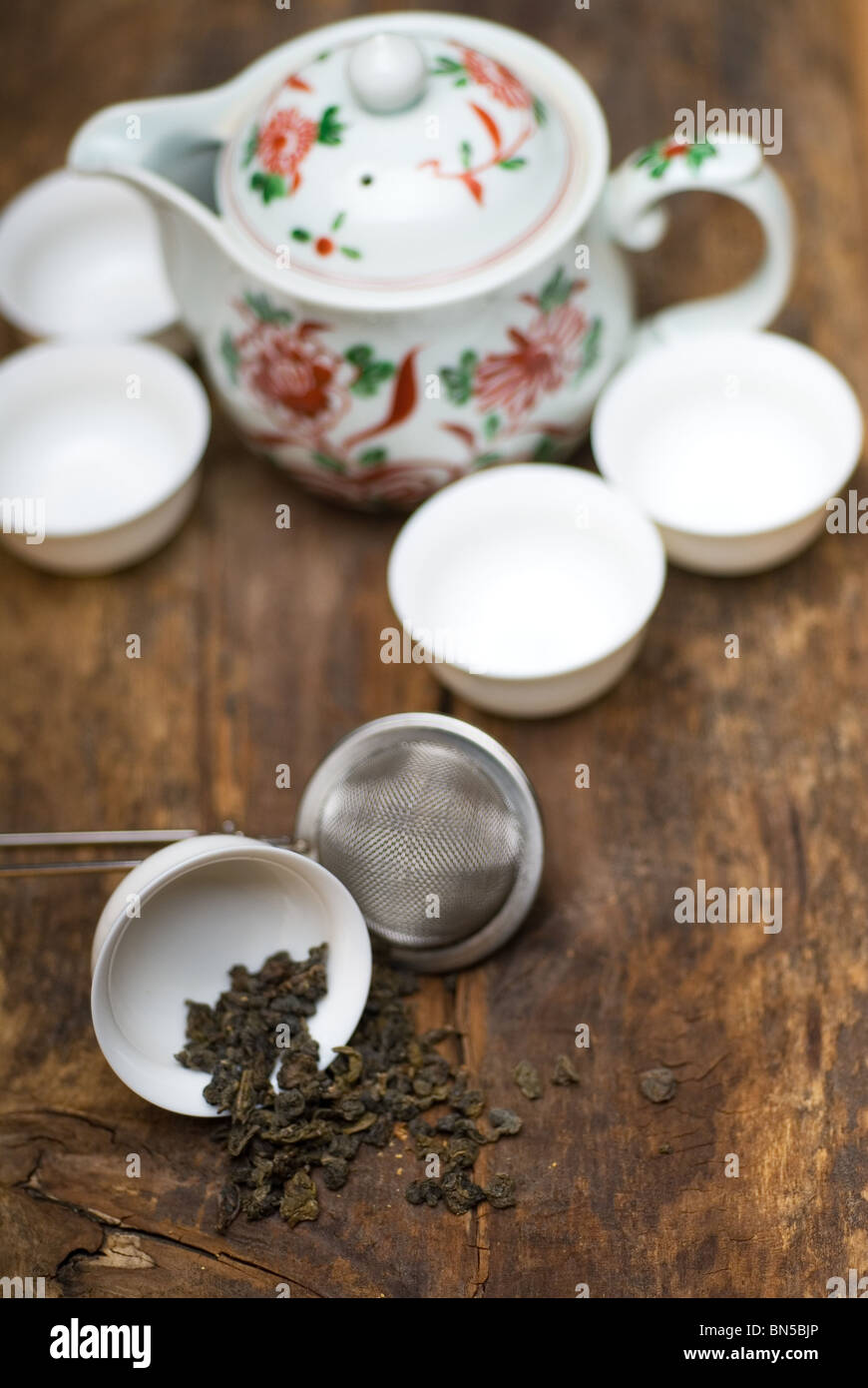 trockenen grünen chinesischen Tee-Set, mit Sieb Closeup, Tassen und Teekanne auf Hintergrund über alte Holzplatte Stockfoto