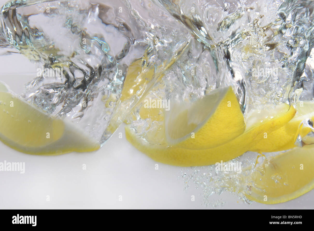 Eine Studioaufnahme von Zitronenspalten ins Wasser gefallen Stockfoto