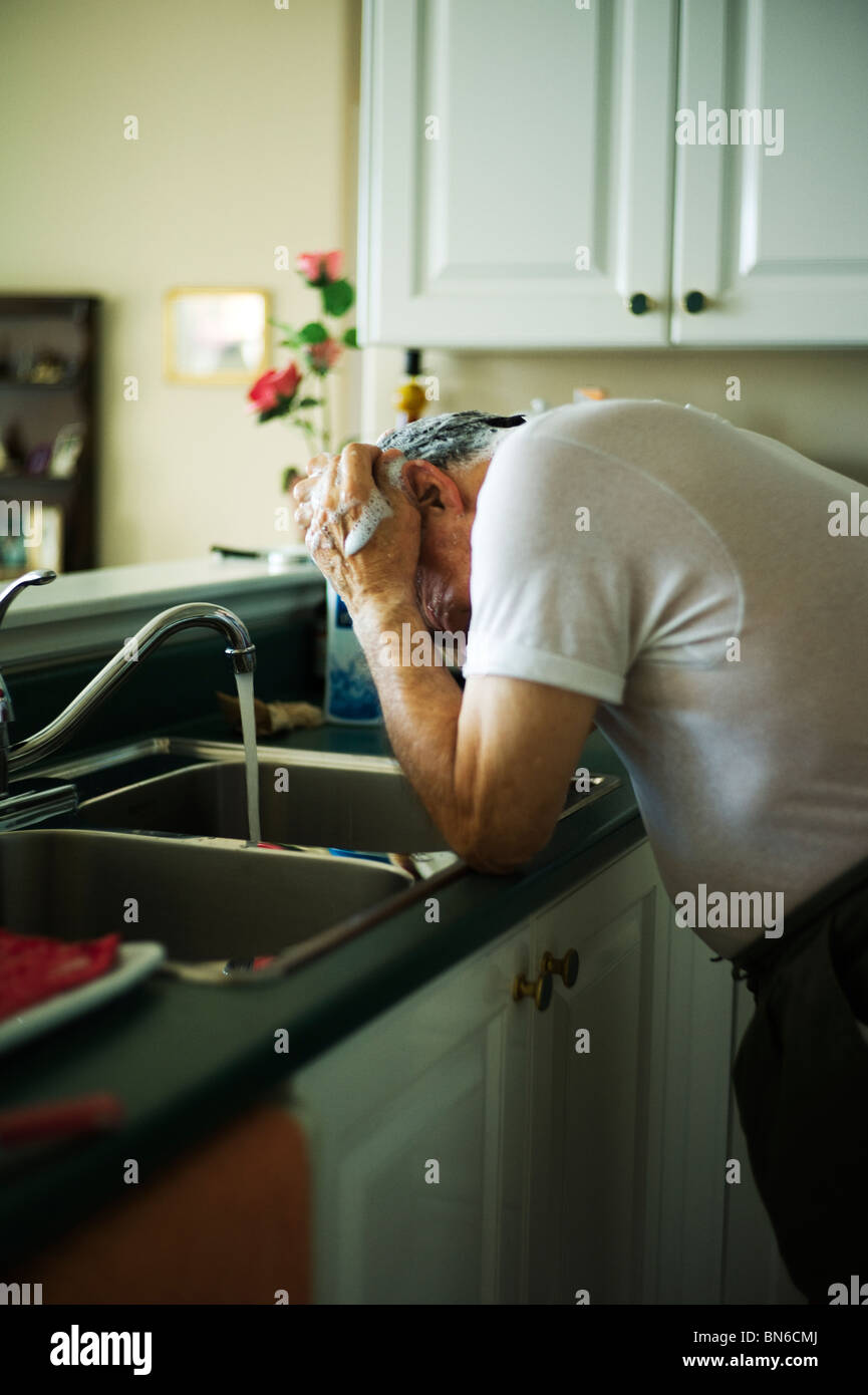 Alter Mann im weißen Unterhemd wäscht Haare bei Küchenspüle. Stockfoto
