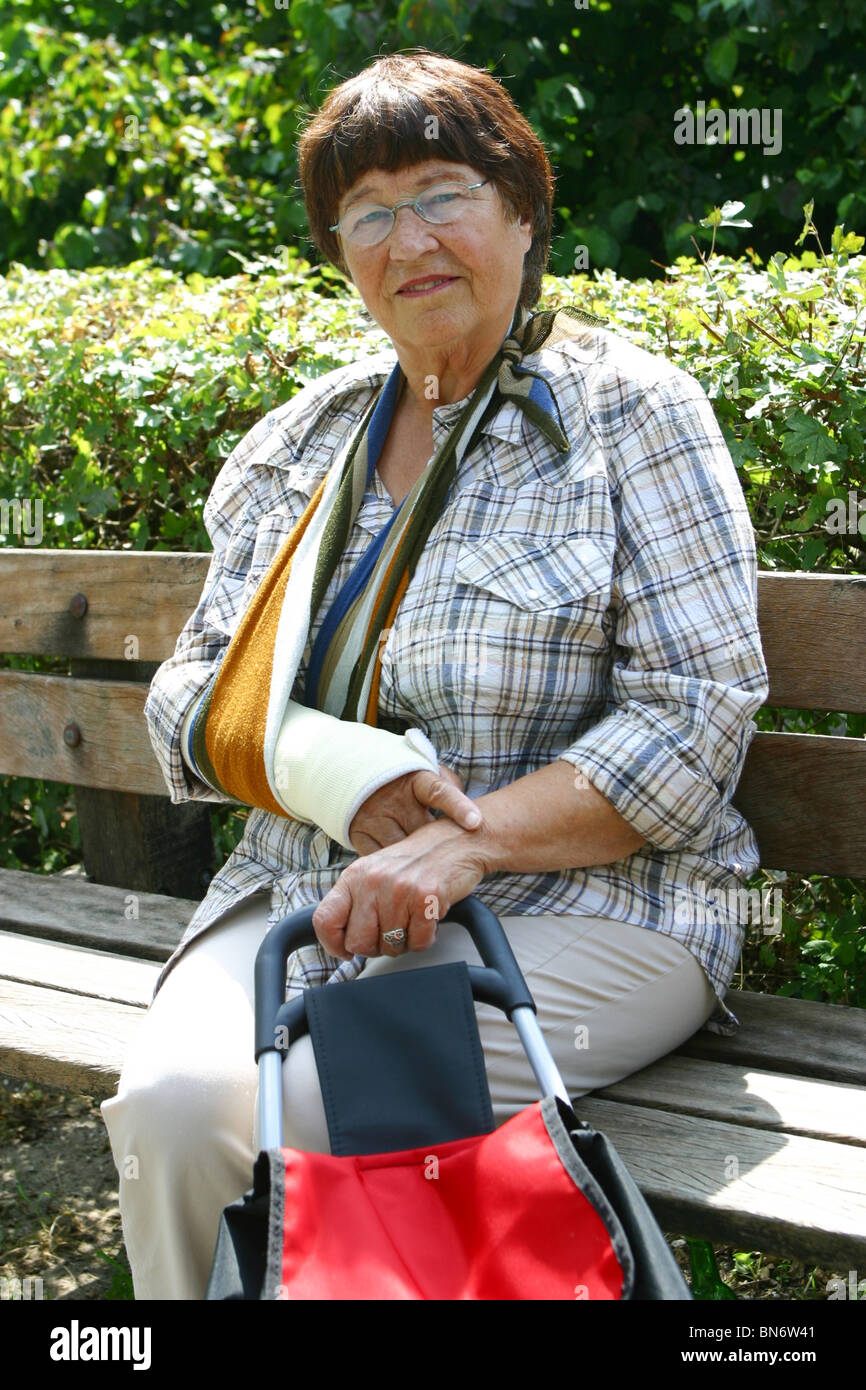 Rentner mit Fraktur der Arm in der Schlinge Sit Parkbank Stockfoto