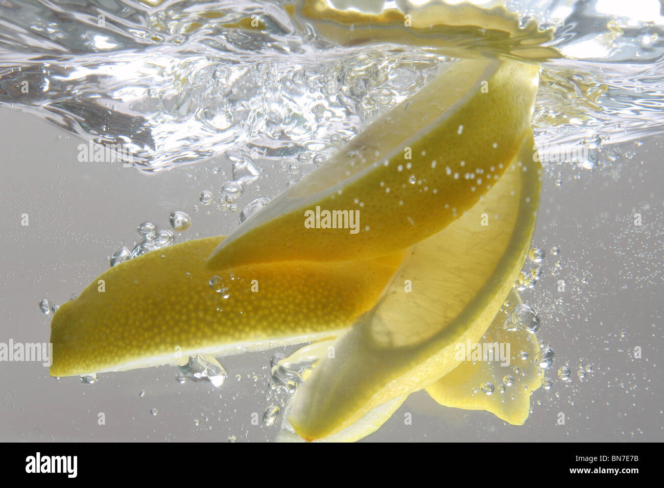 Eine Studioaufnahme von Zitronenspalten ins Wasser gefallen Stockfoto